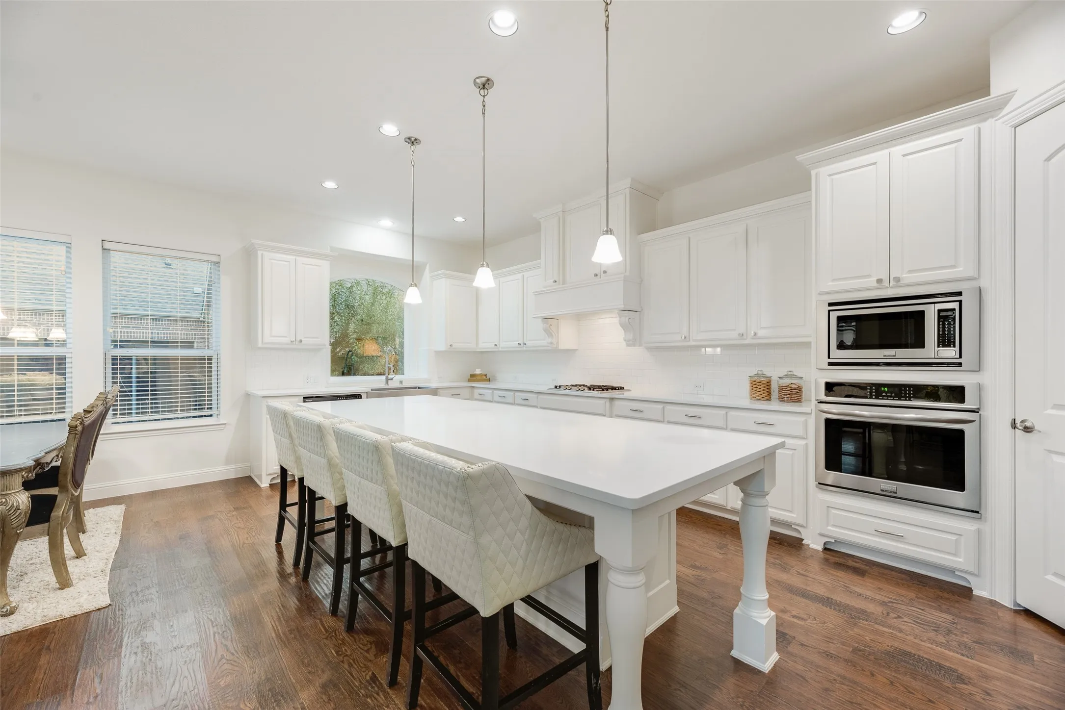 Expansive kitchen featuring a large central island, white cabinetry, integrated stainless steel appliances, dark wood-finish flooring, and recessed lighting