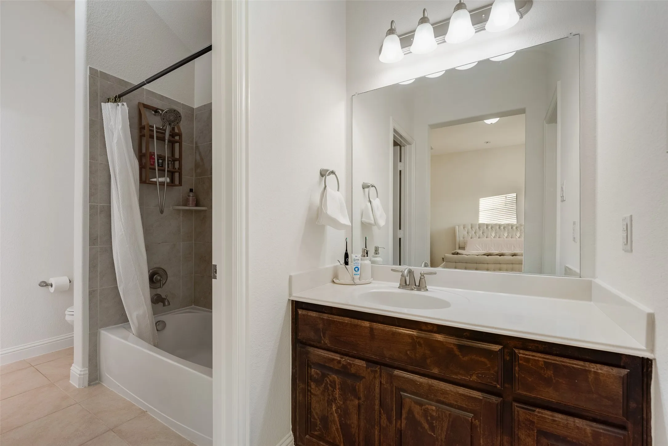Jack and Jill Bathroom. Bathtub with tiled shower surround, single vanity with integrated sink, dark wood-finish cabinetry, and overhead vanity lighting