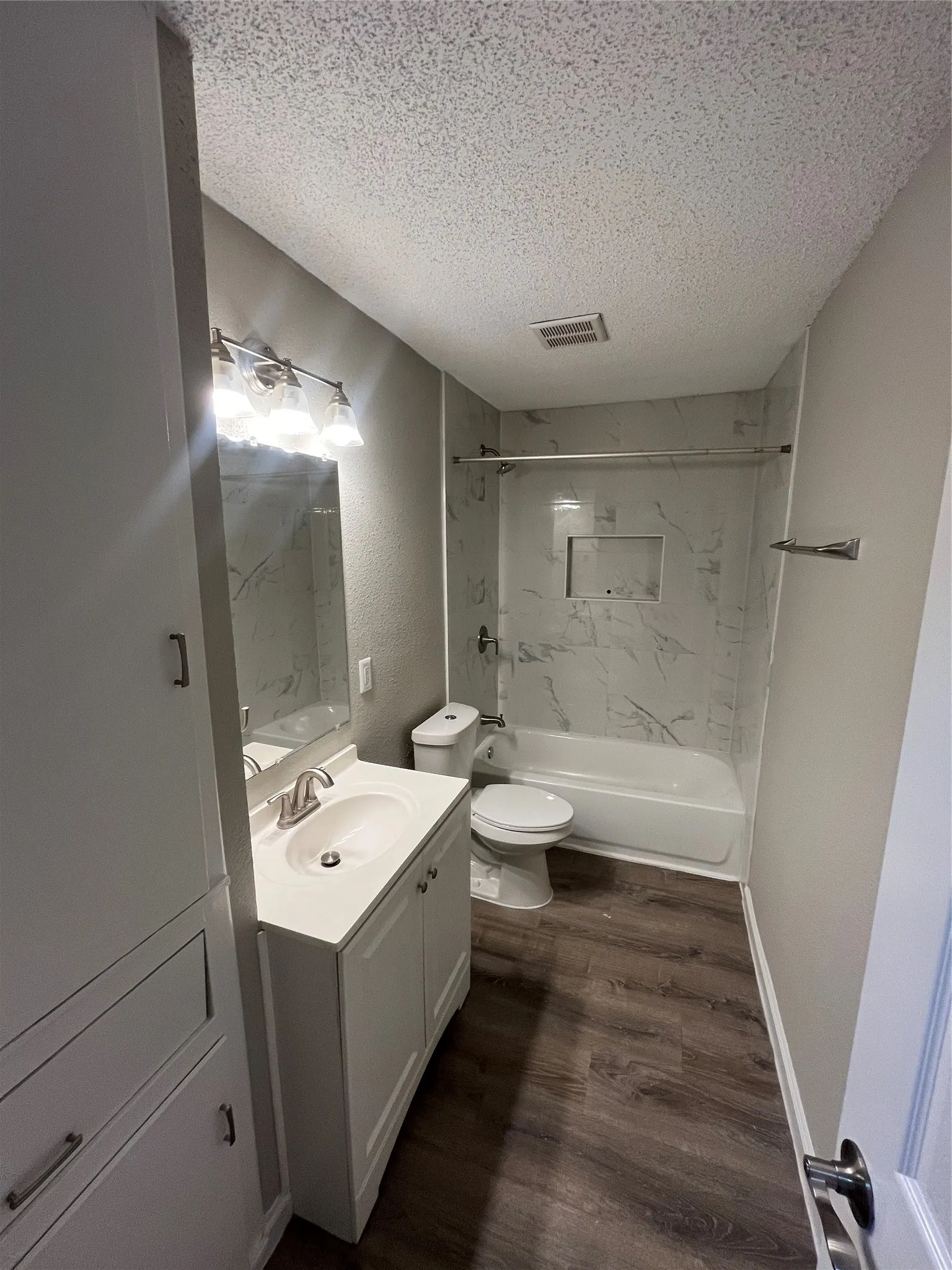 White vanity with an integrated sink and brushed nickel faucet, large built-in white storage cabinetry, and wood-finish flooring