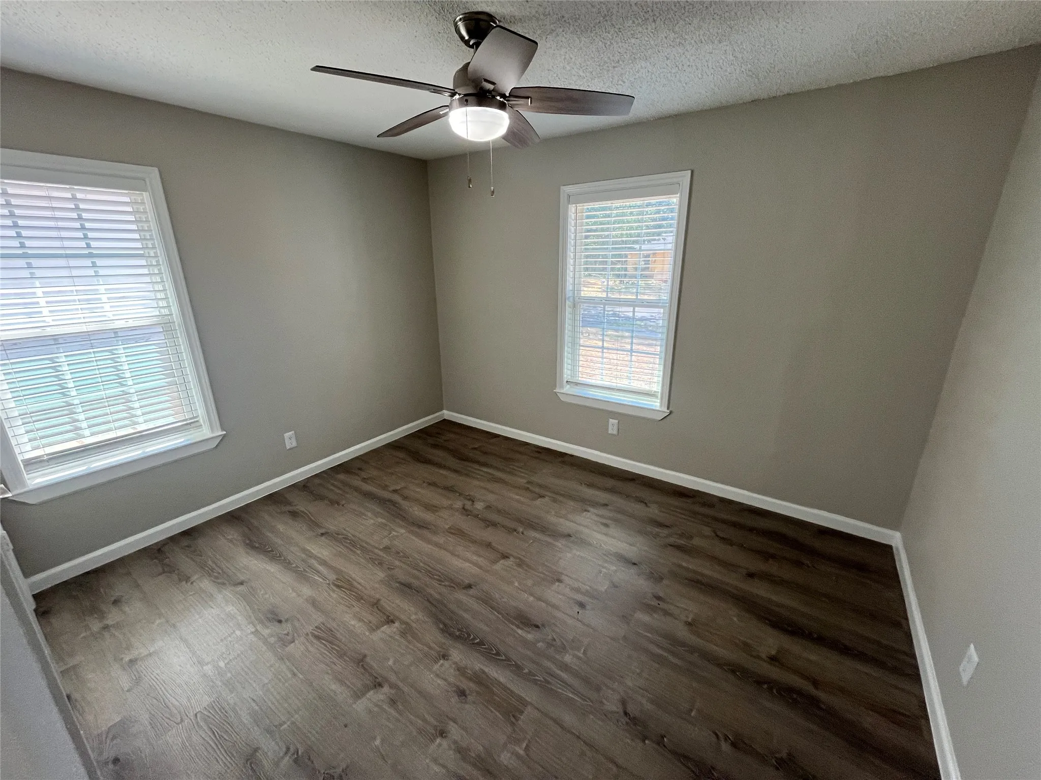 Wood-finish flooring, neutral wall tones, two windows with blinds, and a ceiling fan with integrated lighting