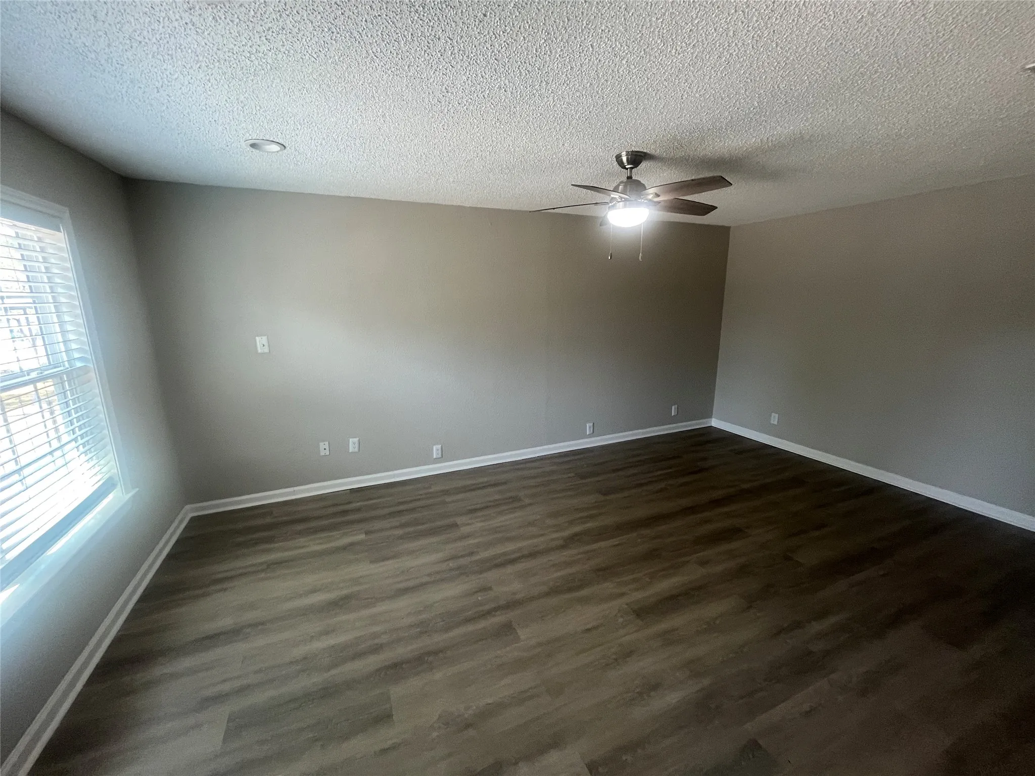Spacious room featuring wood-finish flooring, neutral-toned walls, a ceiling fan with integrated lighting, and recessed ceiling lighting