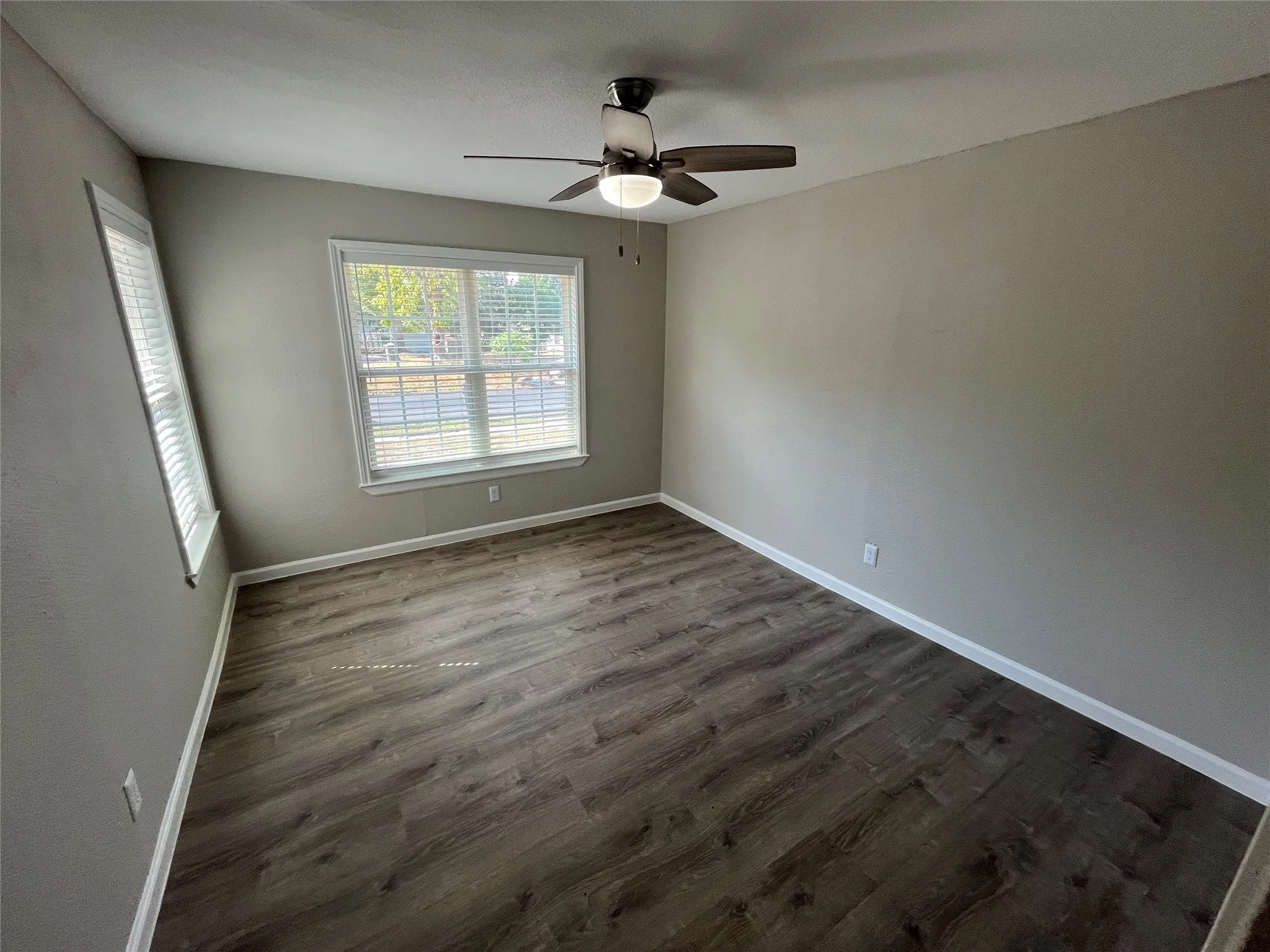 Wood-finish flooring, two windows with blinds, ceiling fan with integrated lighting, and neutral wall tones