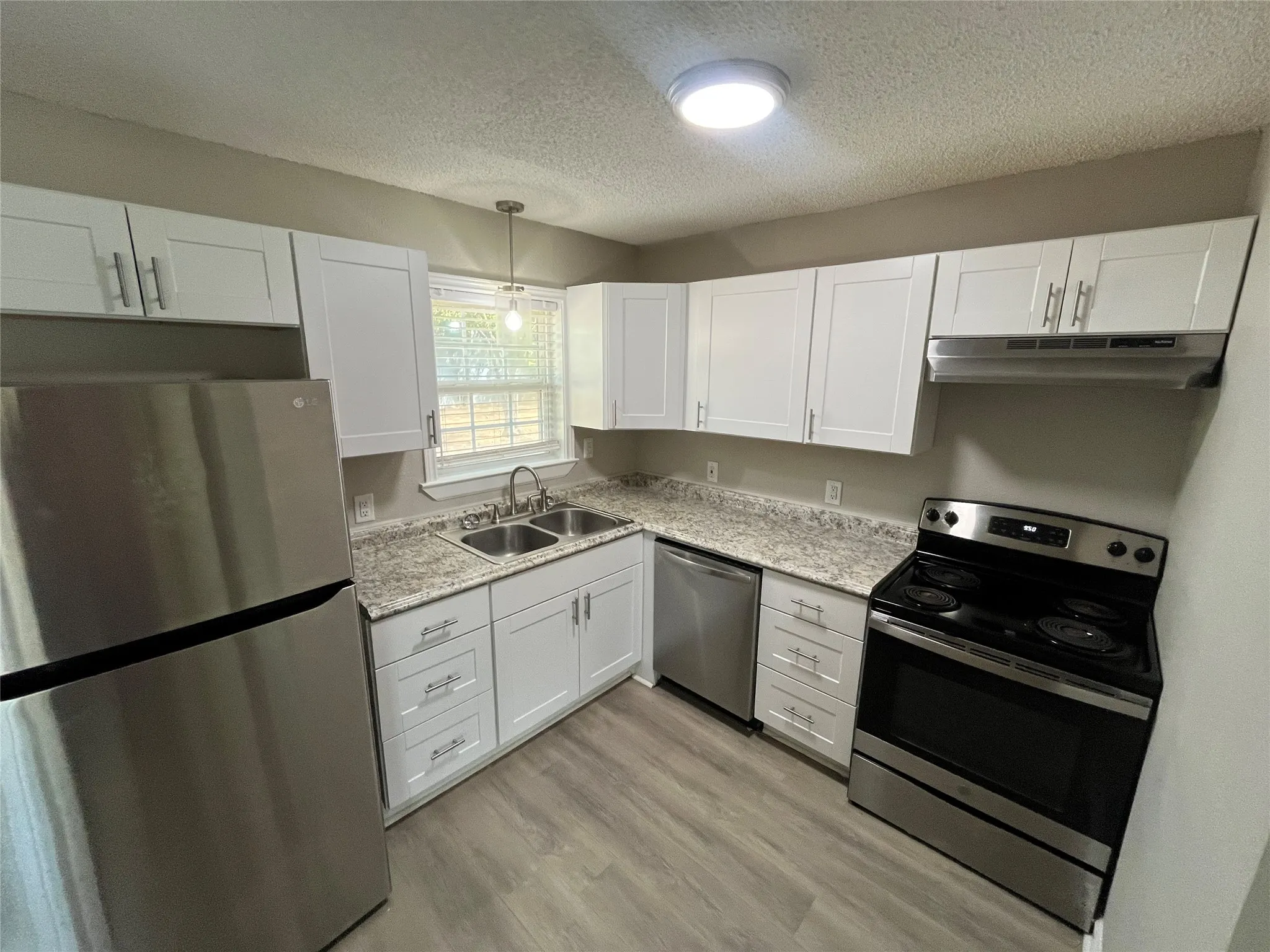 White shaker-style cabinetry, light-toned countertops, stainless steel appliances, dual basin sink, and wood-finish flooring