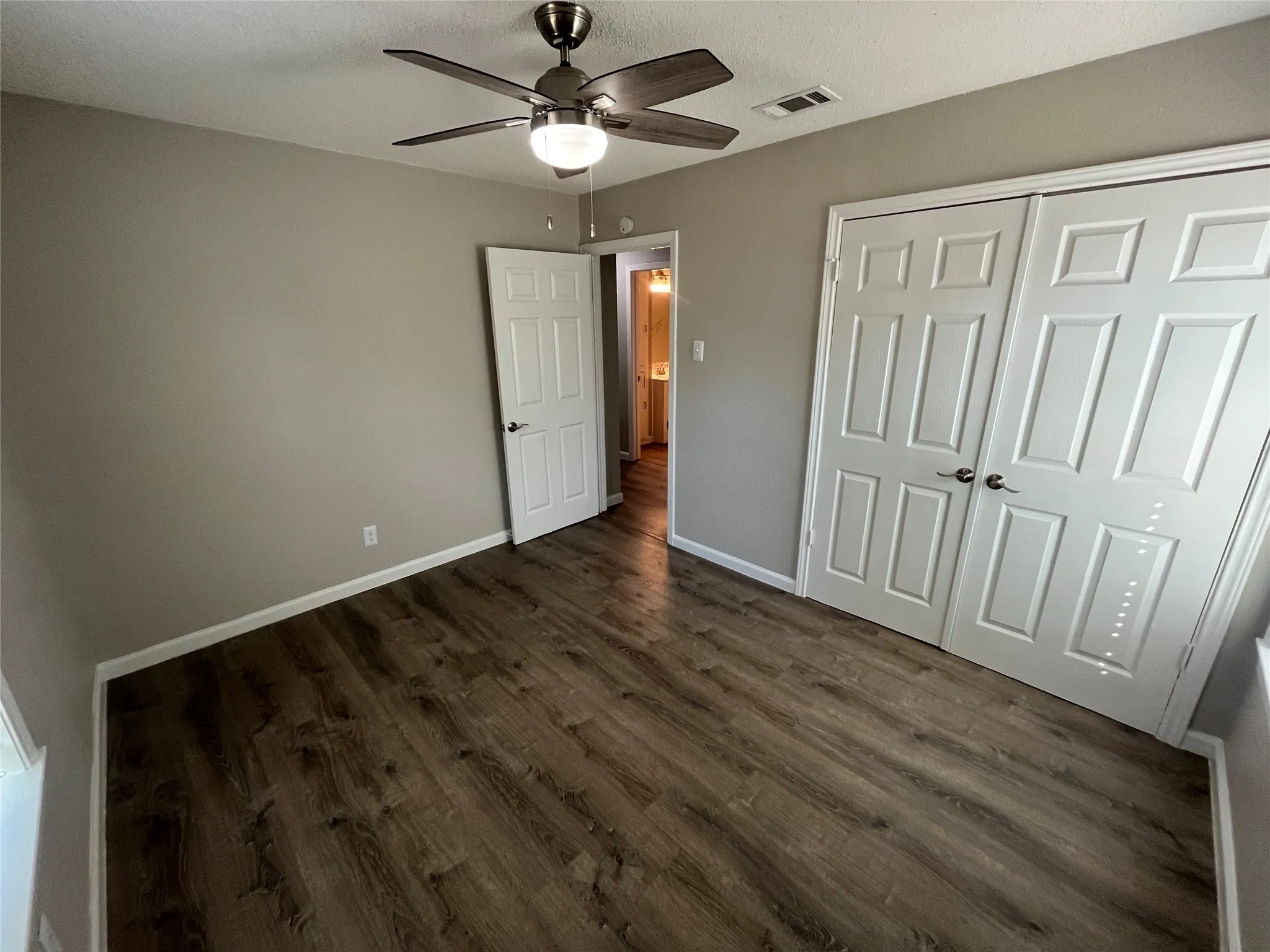 Wood-finish flooring, neutral wall tones, ceiling fan with integrated lighting, and white paneled doors