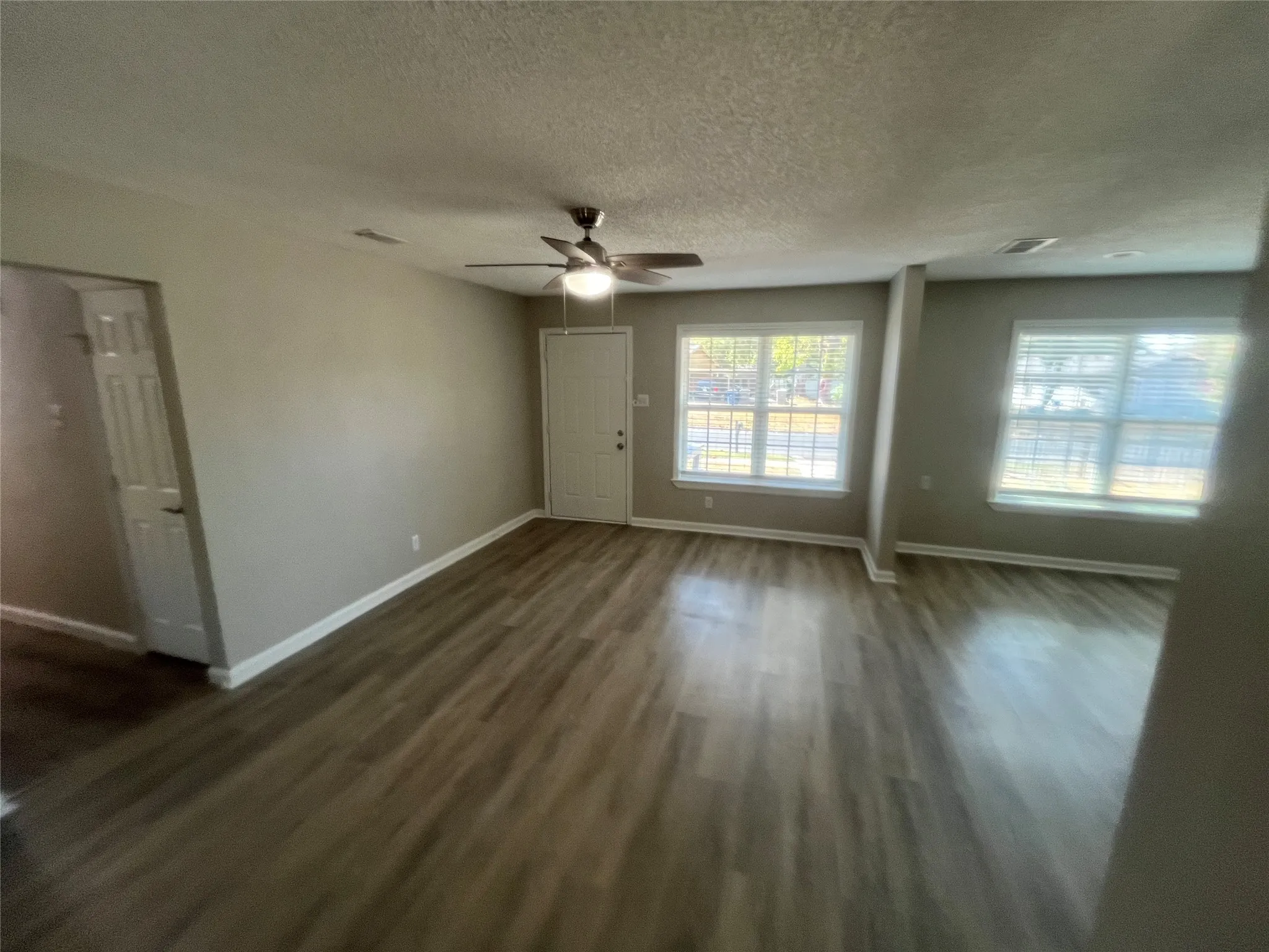 Spacious interior featuring wood-finish flooring, neutral wall tones, multiple windows with blinds, and a ceiling fan with integrated lighting