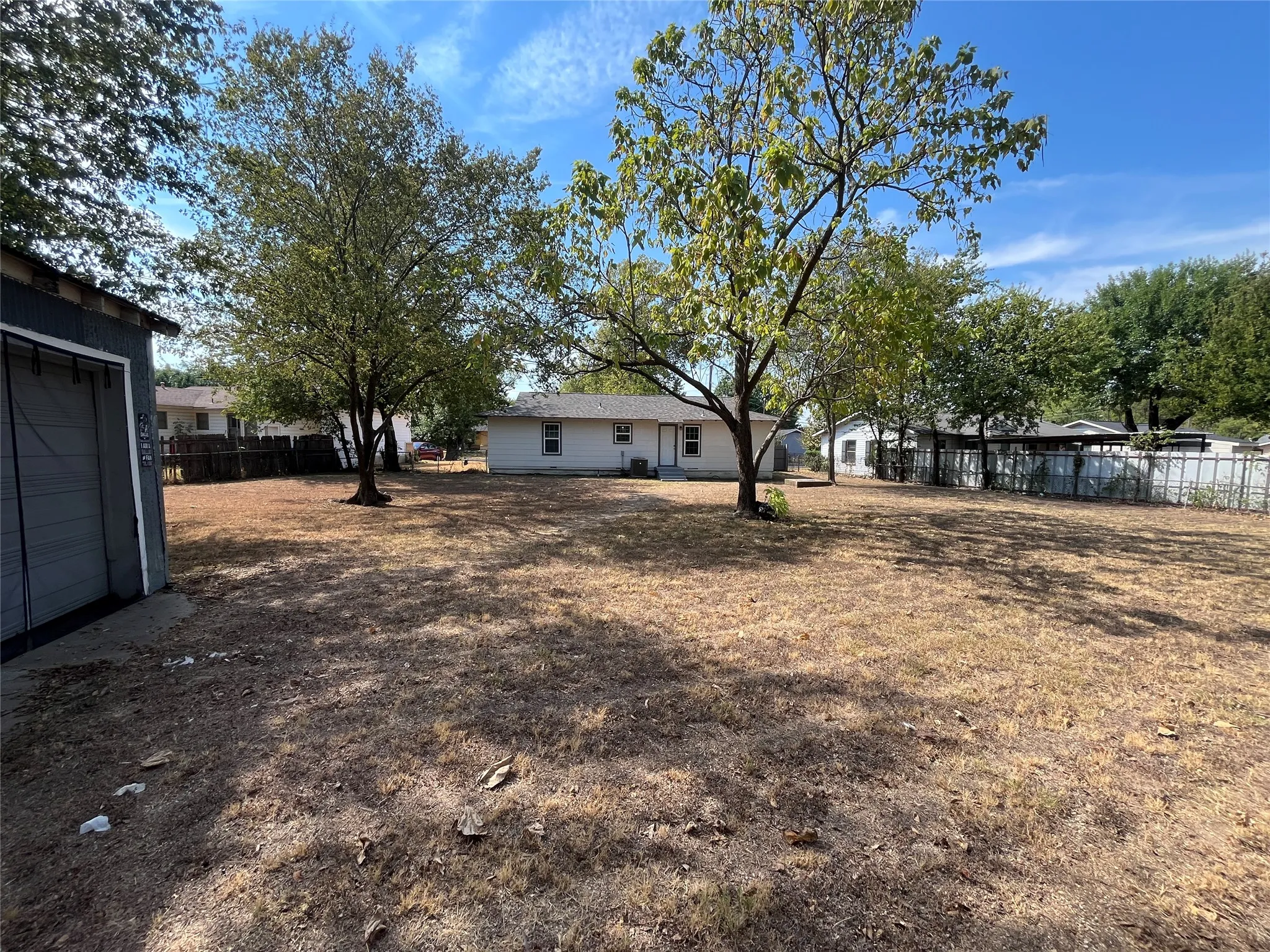 Expansive backyard space featuring mature trees and a detached storage shed
