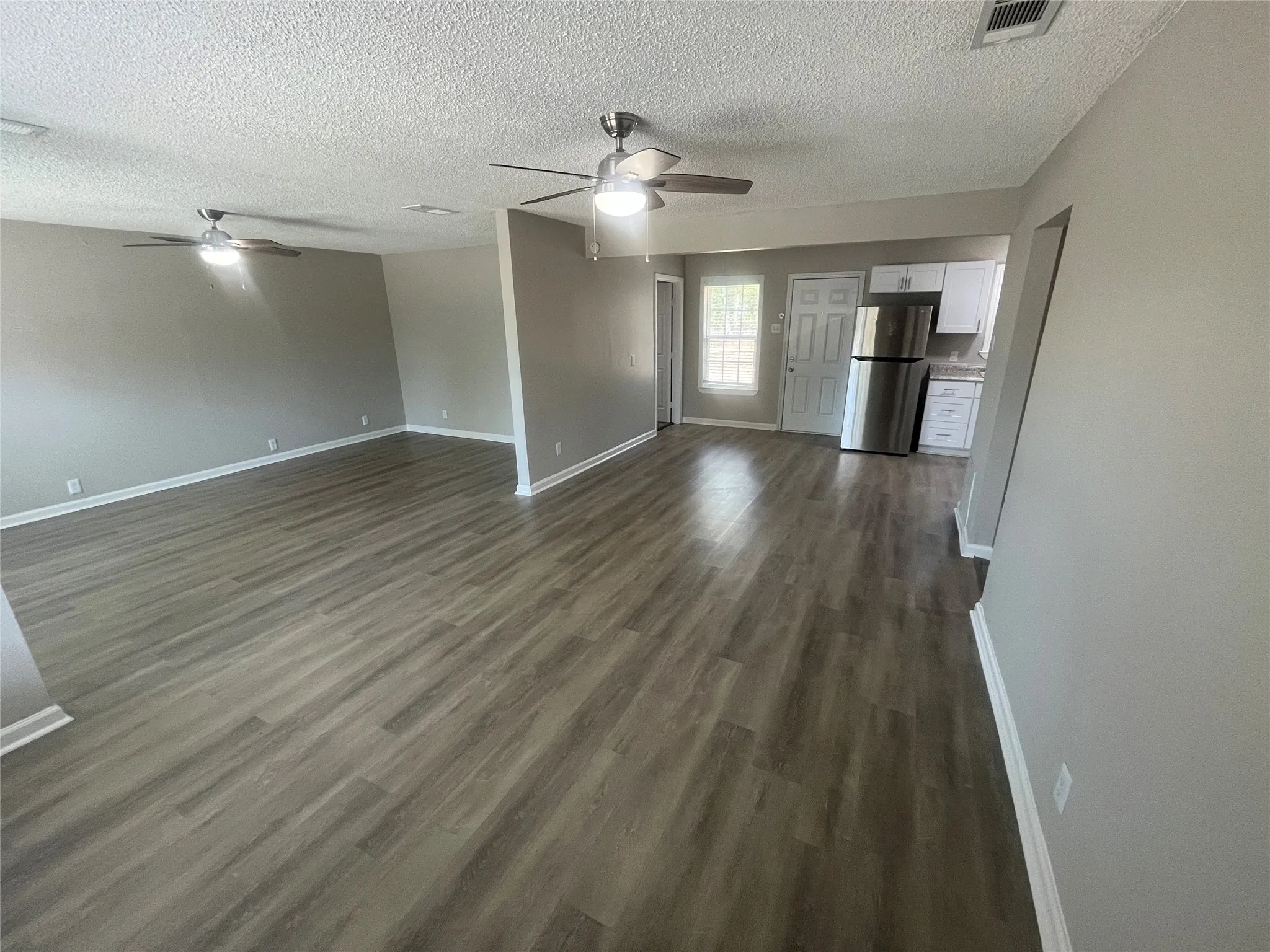 Expansive common area featuring wood-finish flooring, neutral paint tones, and ceiling fans