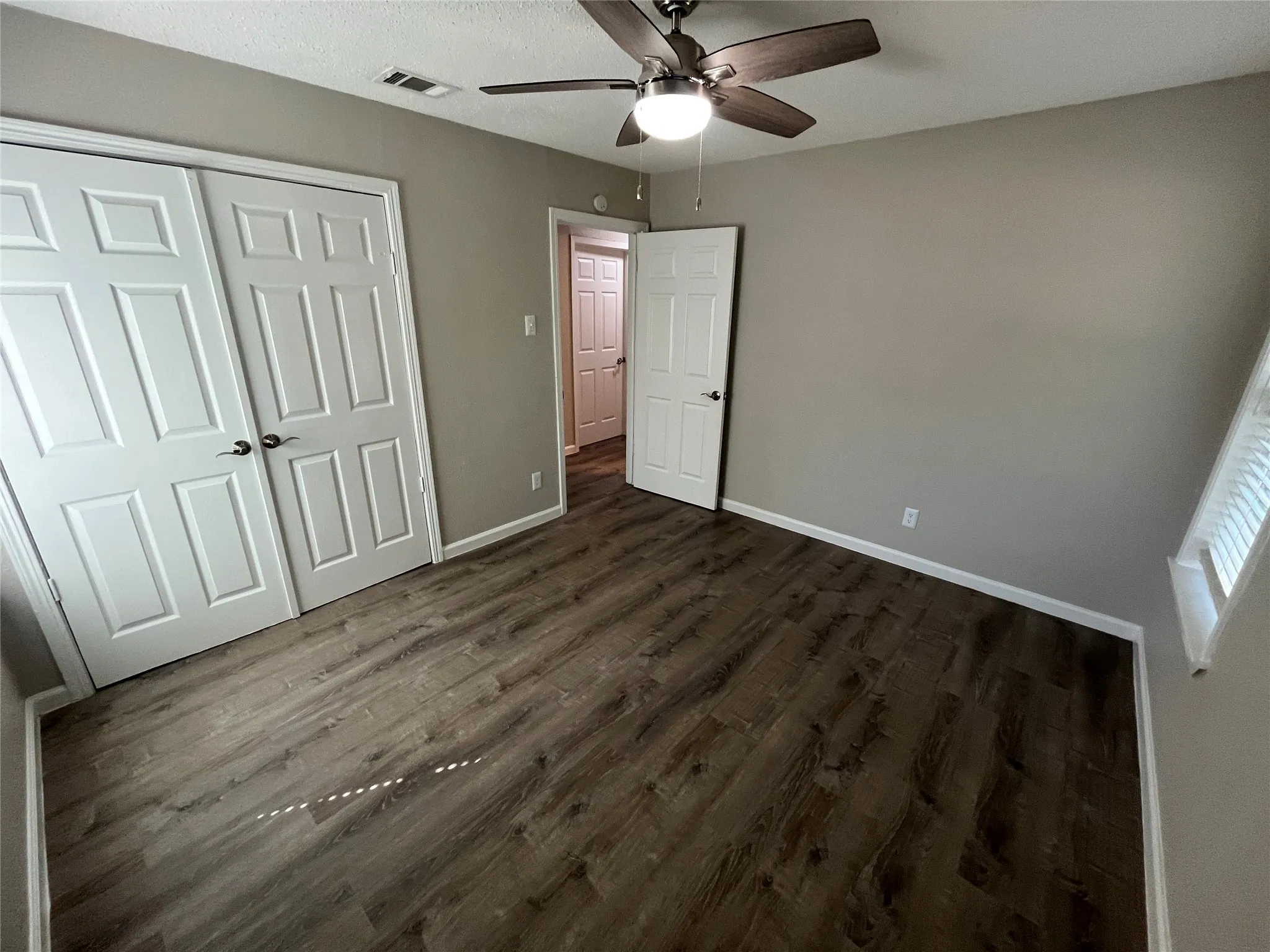 Wood-finish flooring throughout, ceiling fan with integrated lighting, neutral wall tones, white trim, and a white paneled door