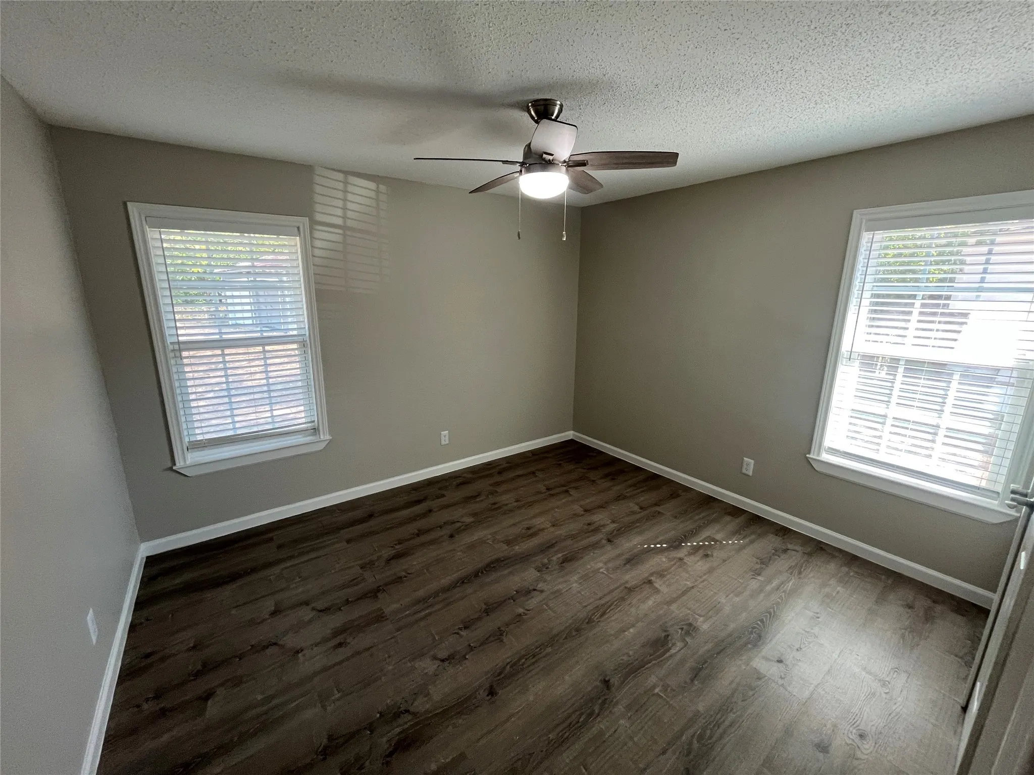 Wood-finish flooring, two windows with white blinds, and a ceiling fan with integrated lighting