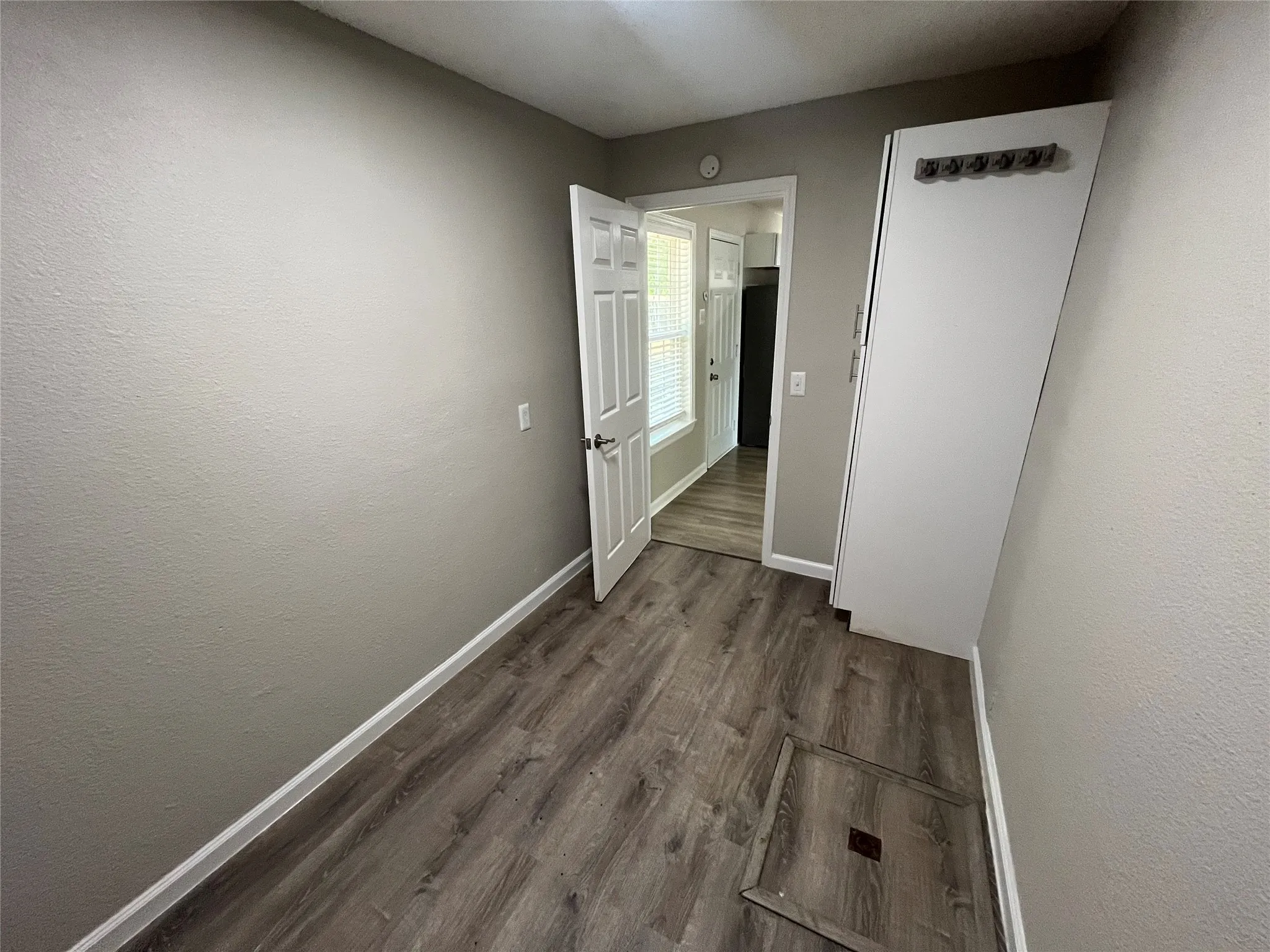 Wood-finish flooring with white baseboards, textured walls, and a white paneled door