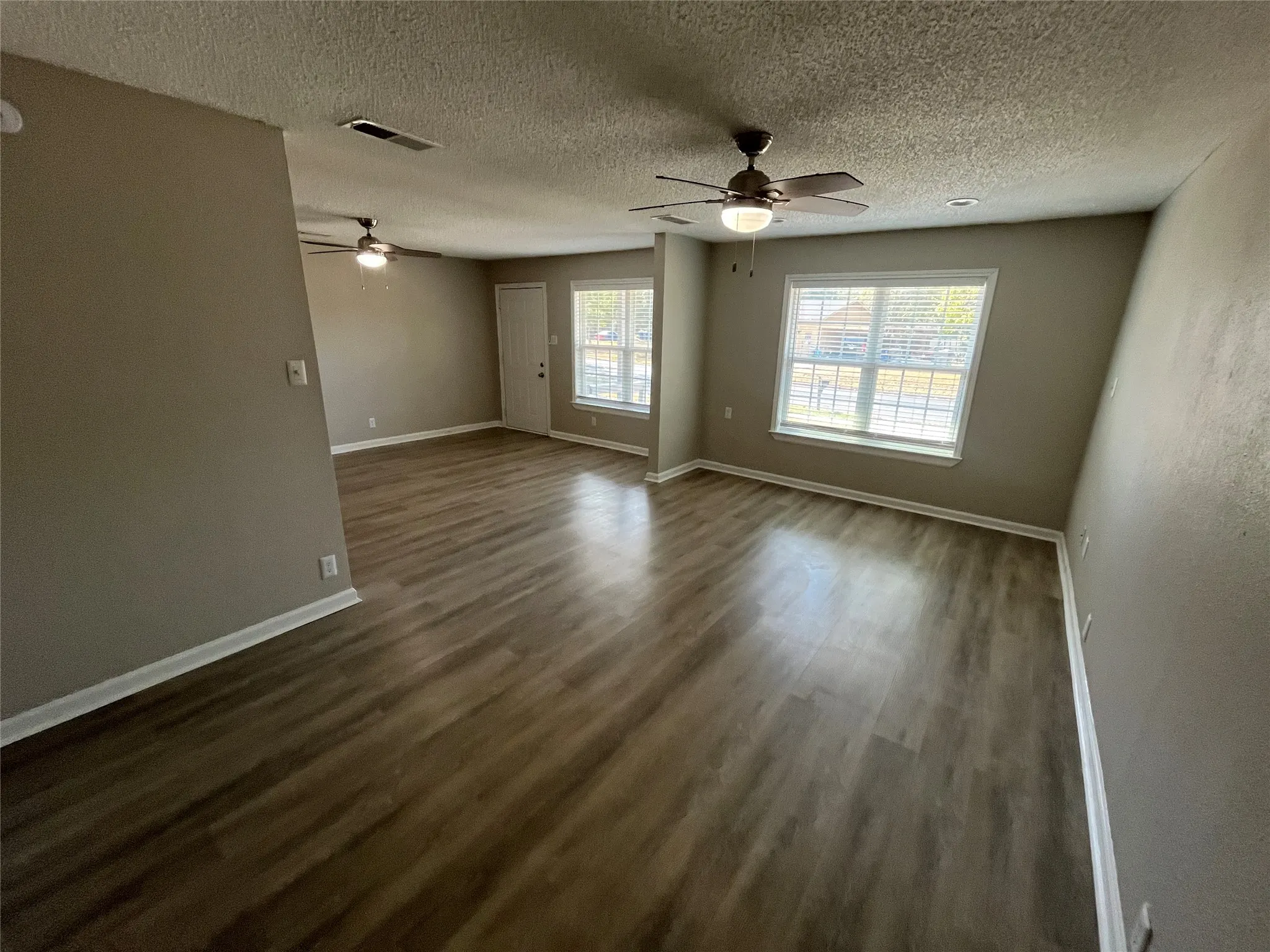 Spacious interior featuring wood-finish flooring, neutral wall tones, multiple windows, and two ceiling fans with integrated lighting