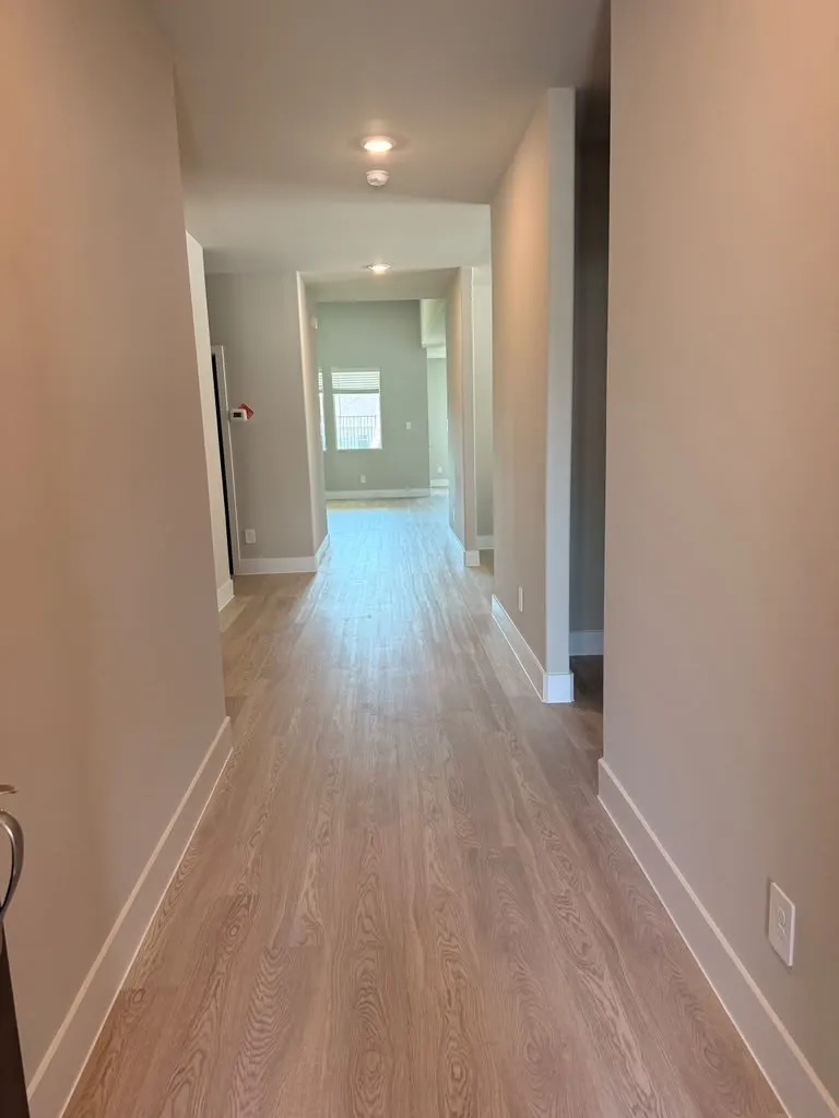 Recessed lighting illuminates wood-finish flooring throughout the hallway