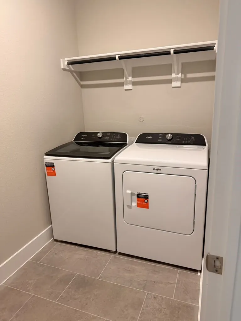 Laundry area featuring a top-load washer, front-load dryer, tile flooring, and integrated shelving with a hanging rod