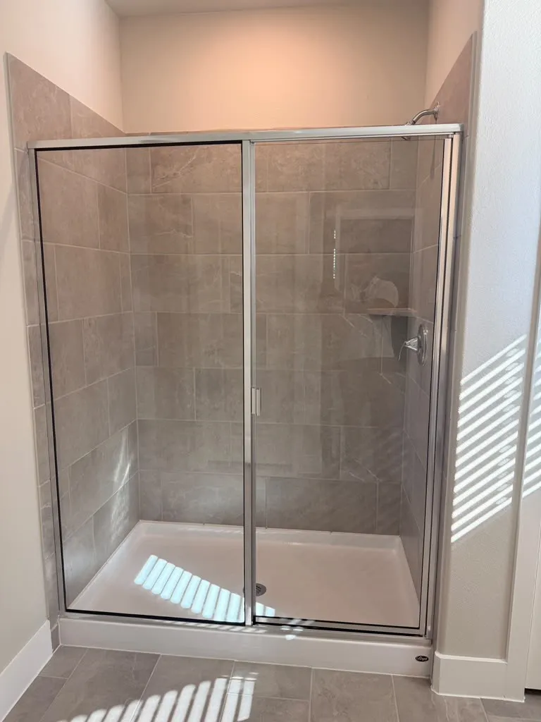 Enclosed shower with sliding glass doors, neutral-toned tile surround, built-in shelving, white shower pan, and coordinating floor tile