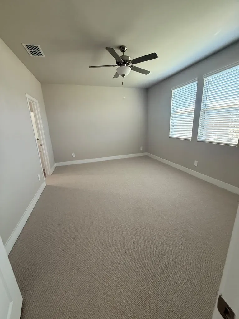 Carpeted room featuring a ceiling fan with integrated lighting, two windows with blinds, and neutral painted walls