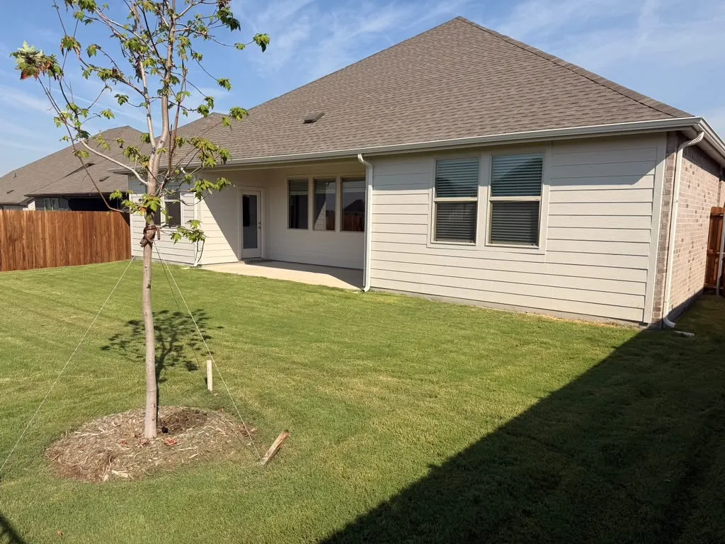 Expansive backyard featuring a manicured lawn, concrete patio, and privacy fencing