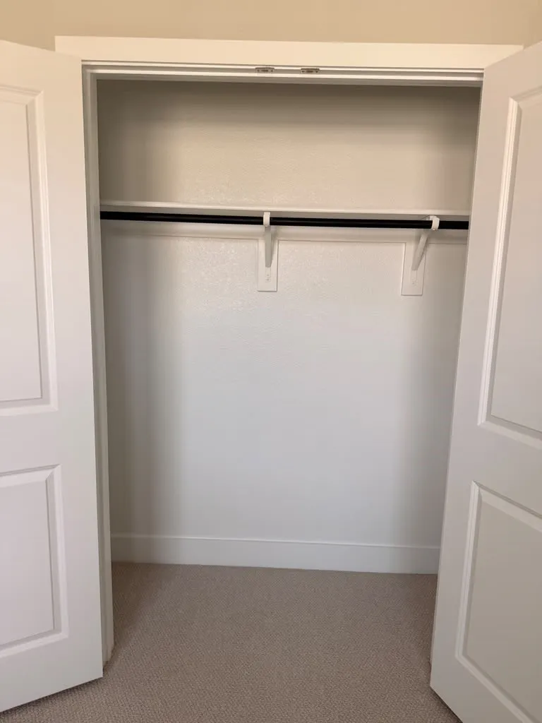 Recessed closet with a single hanging rod, textured wall finish, light-toned carpet, and panel doors