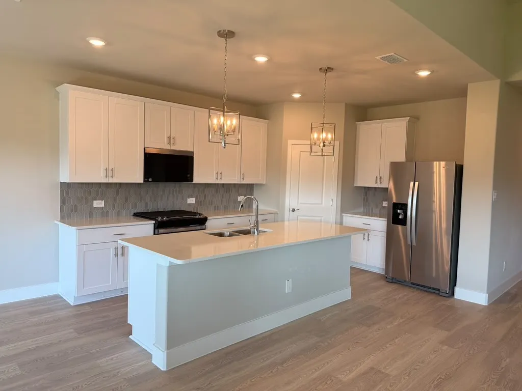 White cabinetry with stainless steel hardware, a kitchen island with an undermount sink, a gray tile backsplash, and stainless steel appliances