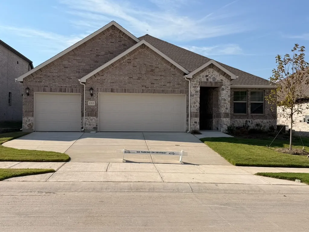 Brick and stone facade with a covered entry, two-car garage, and manicured landscaping