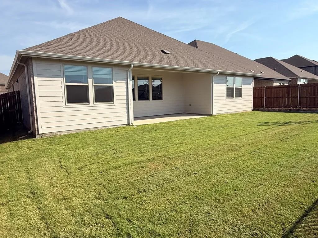 Expansive green lawn with a concrete patio and full privacy fence