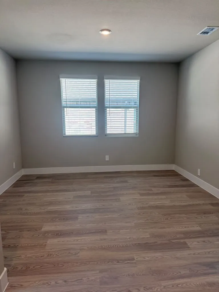 Wood-finish flooring, recessed ceiling light, two windows with blinds, and neutral wall paint