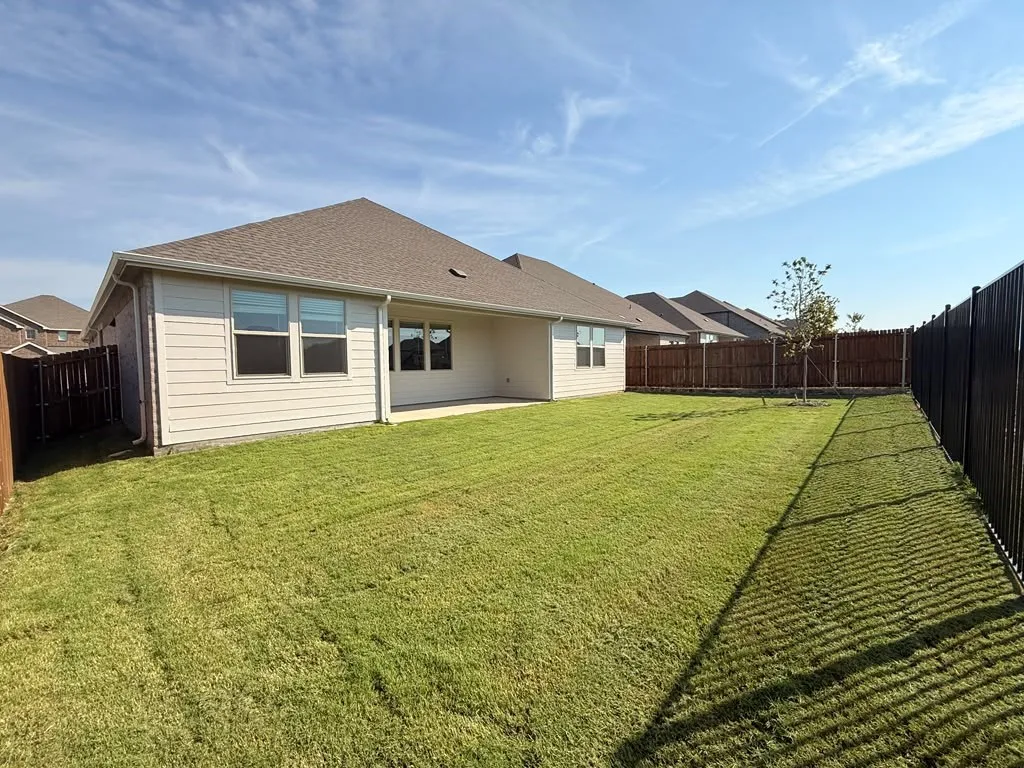 Expansive lawn, concrete patio, tan siding, privacy fencing, and dark shingle roof