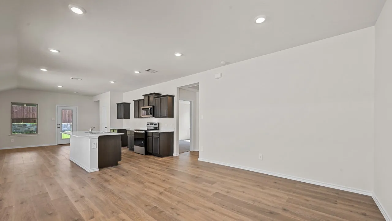 Wood-finish flooring, recessed lighting, vaulted ceiling, kitchen island with sink, and dark cabinetry
