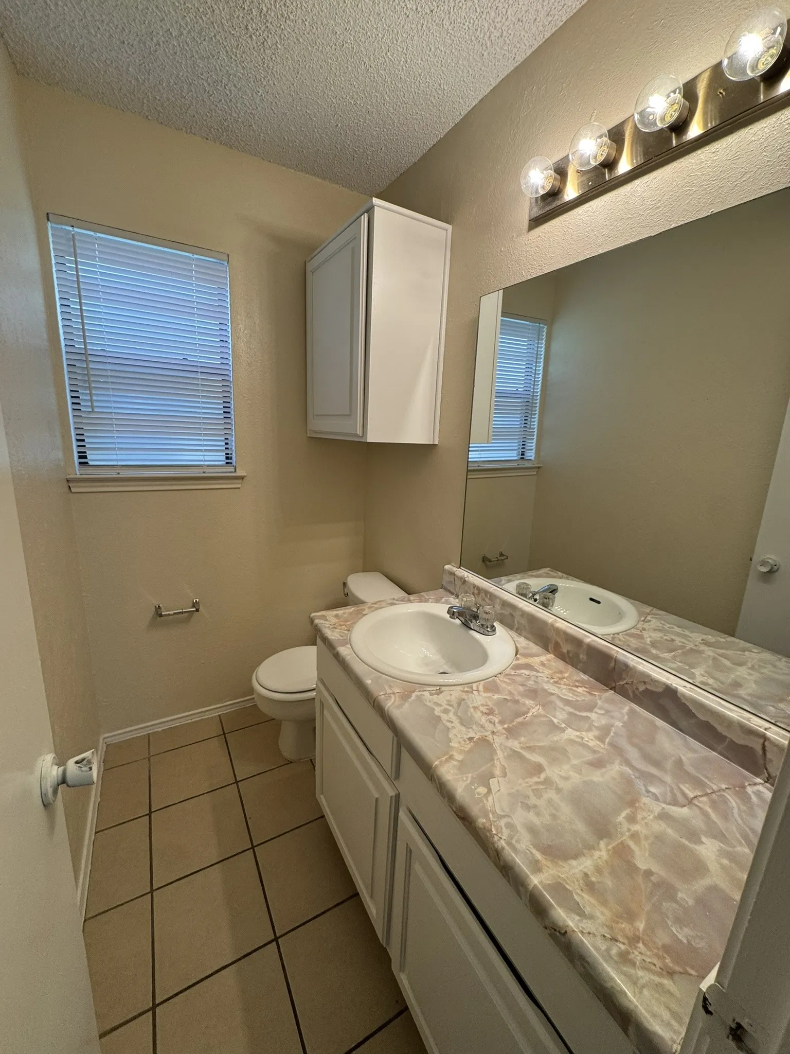 Vanity with integrated sink, expansive mirror, tile flooring, and overhead lighting fixture