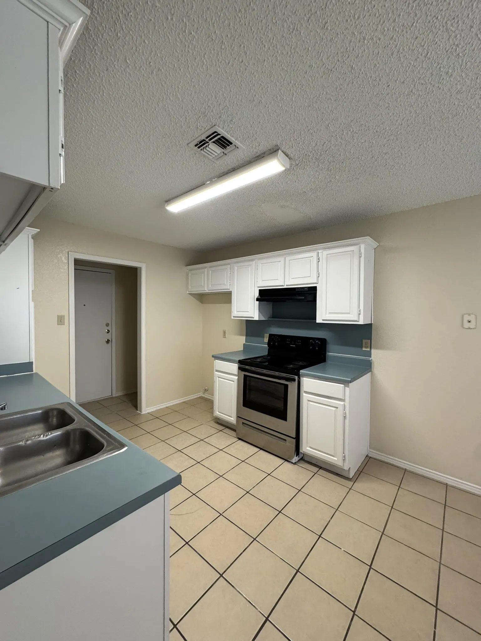 Kitchen featuring white cabinetry, a stainless steel range, a double basin sink, and tile flooring