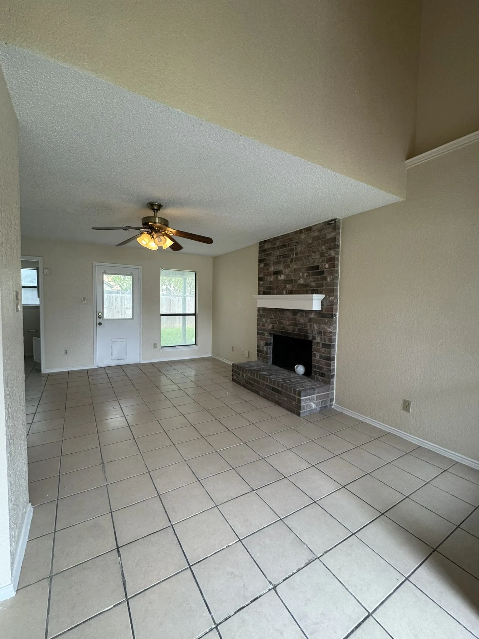 Tile flooring, brick fireplace with mantel, ceiling fan, and abundant natural light