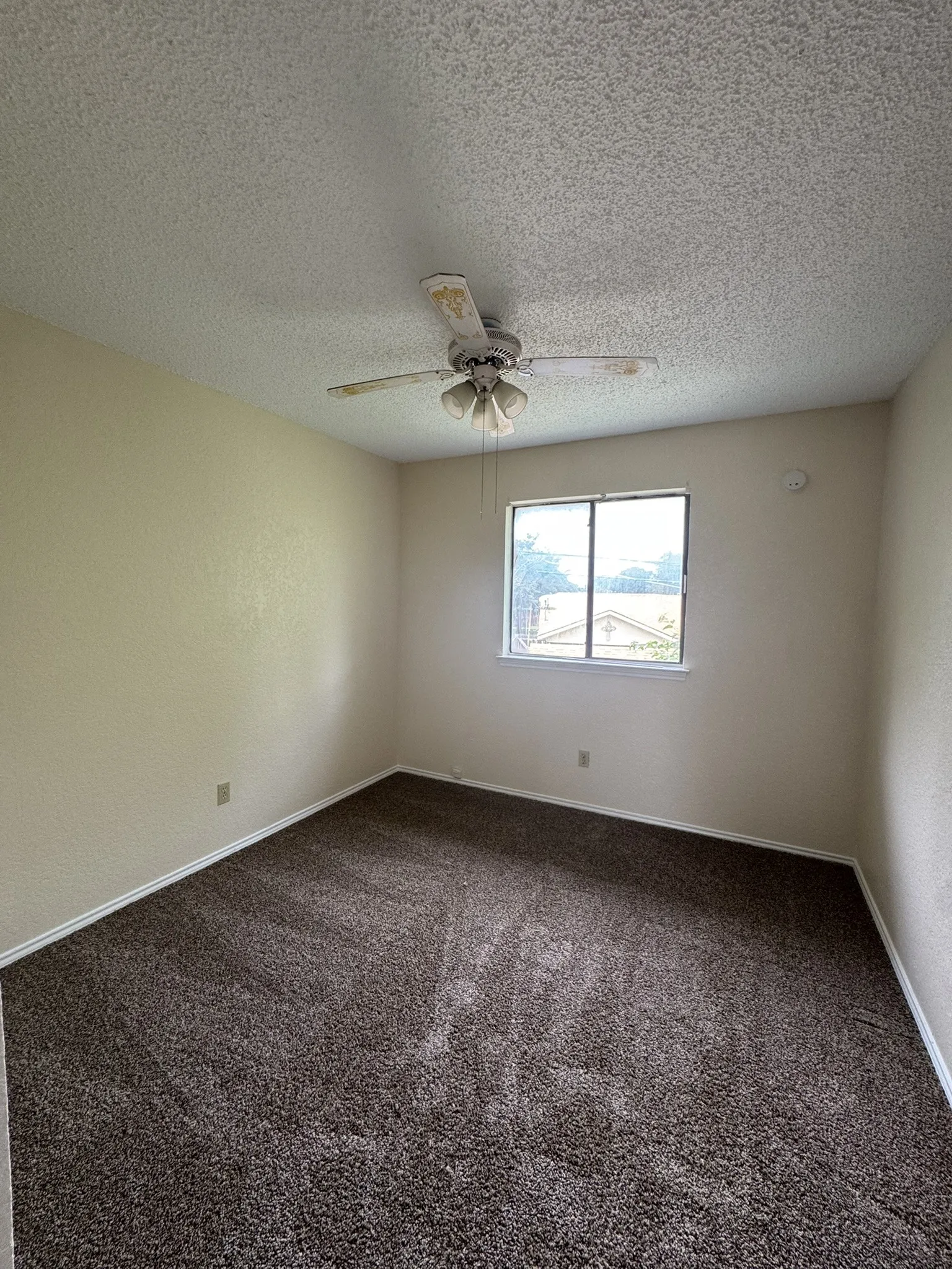 Brown-tone carpeting, window for natural light, and a ceiling fan with integrated lighting