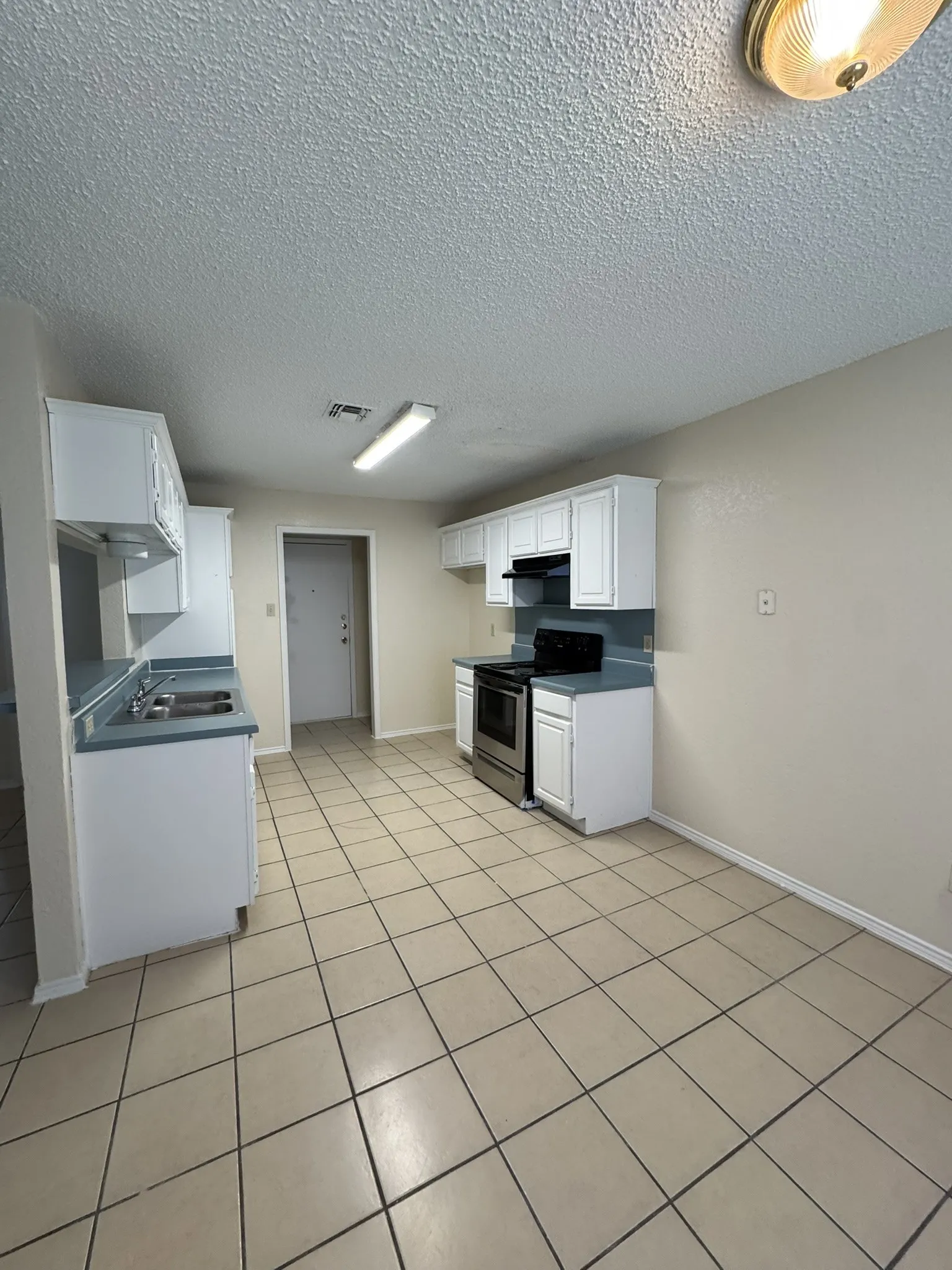 Kitchen featuring tile flooring, white cabinetry, integrated stainless steel range, dual basin sink, and recessed lighting