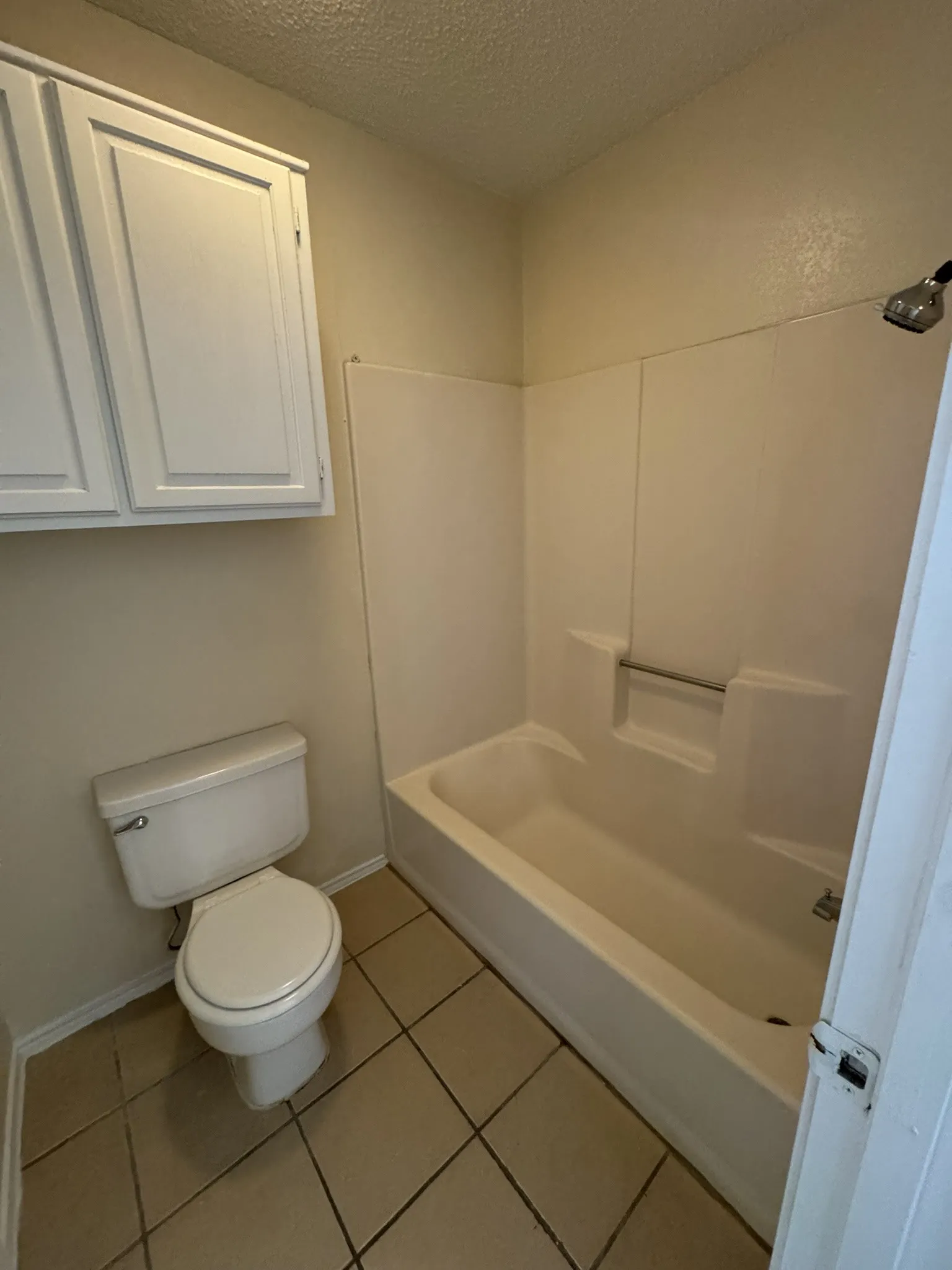 Built-in upper cabinetry, white toilet, and a combination tub and shower unit with a wall-mounted showerhead