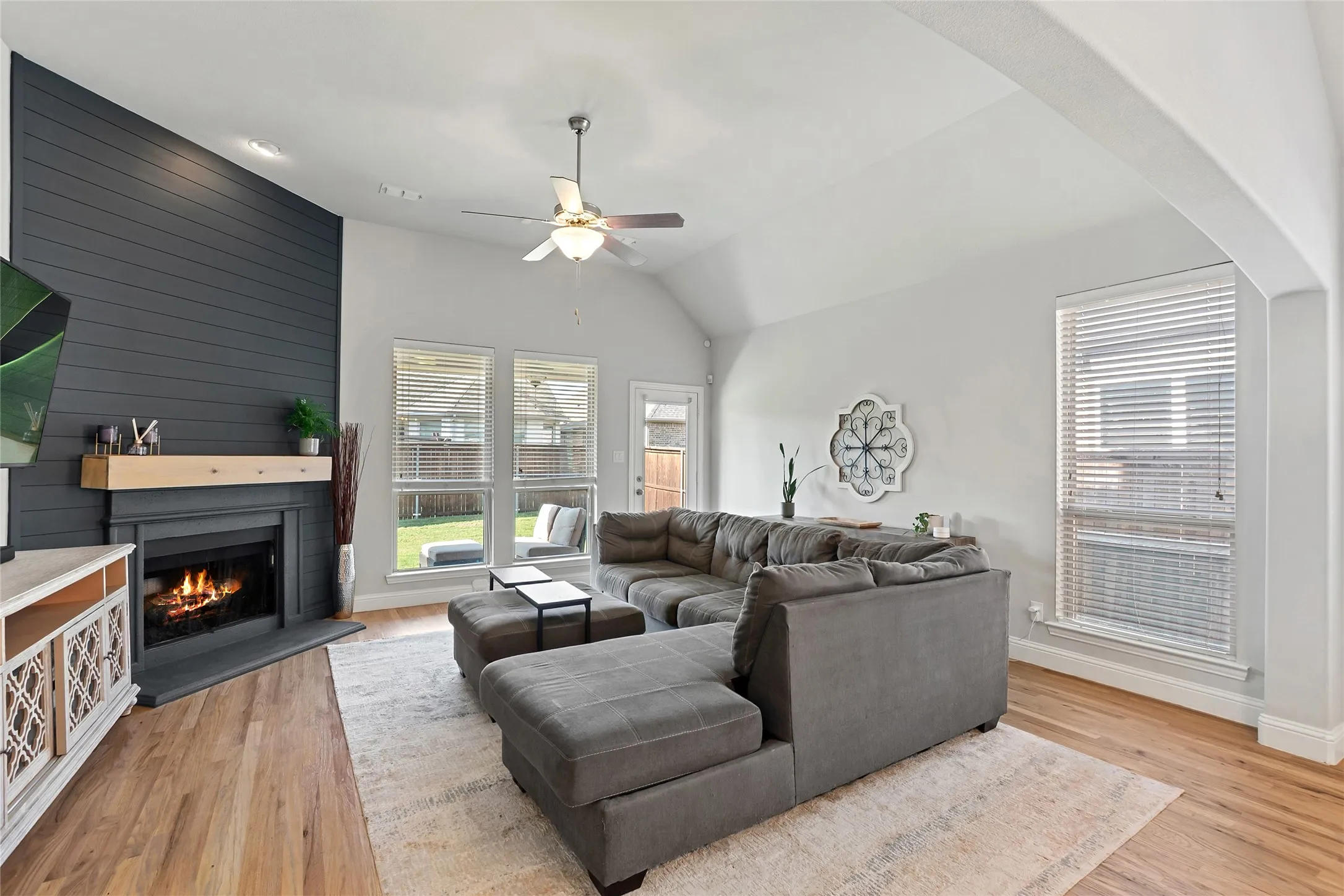 Vaulted ceiling with recessed lighting, wood-finish flooring, fireplace with shiplap-style accent wall, and multiple windows