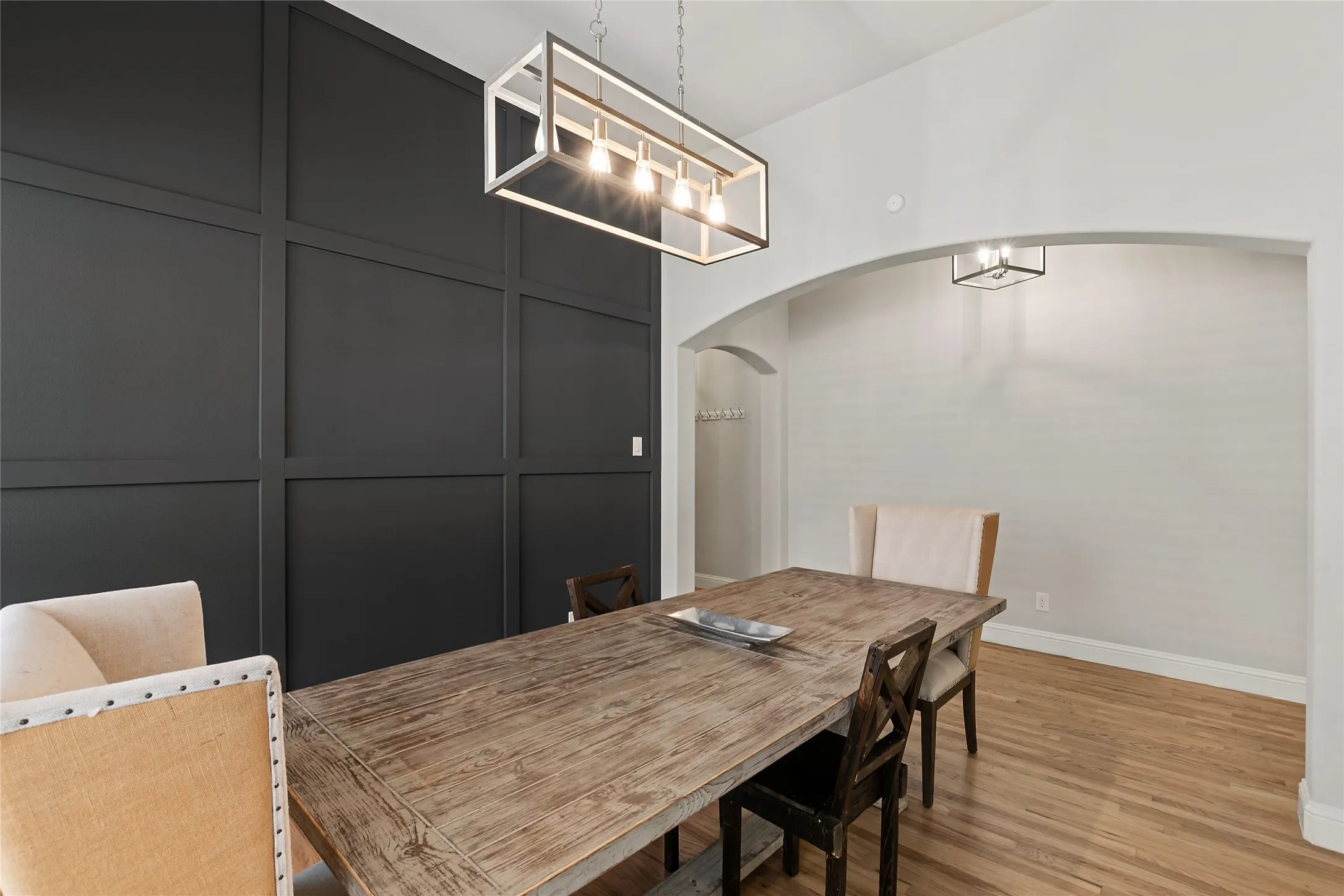 Decorative wall paneling, a rectangular chandelier, arched doorways, and wood-finish flooring