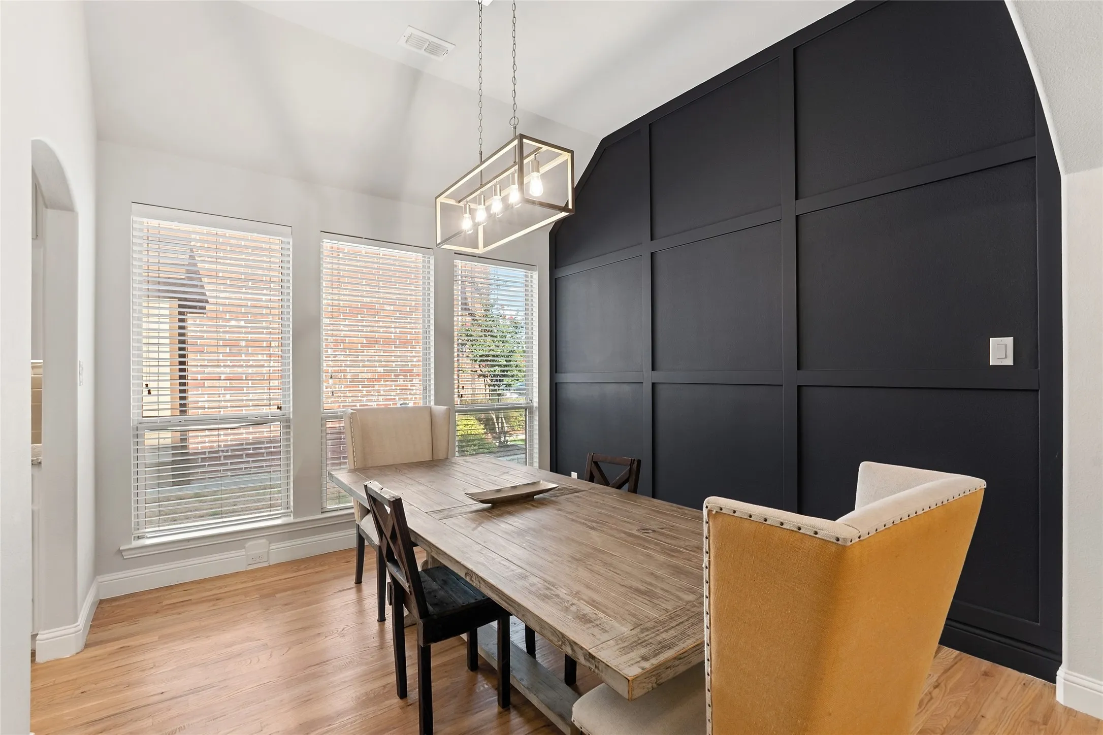 Vaulted ceiling with a linear chandelier, wood-finish flooring, accent wall with panel molding, and triple windows