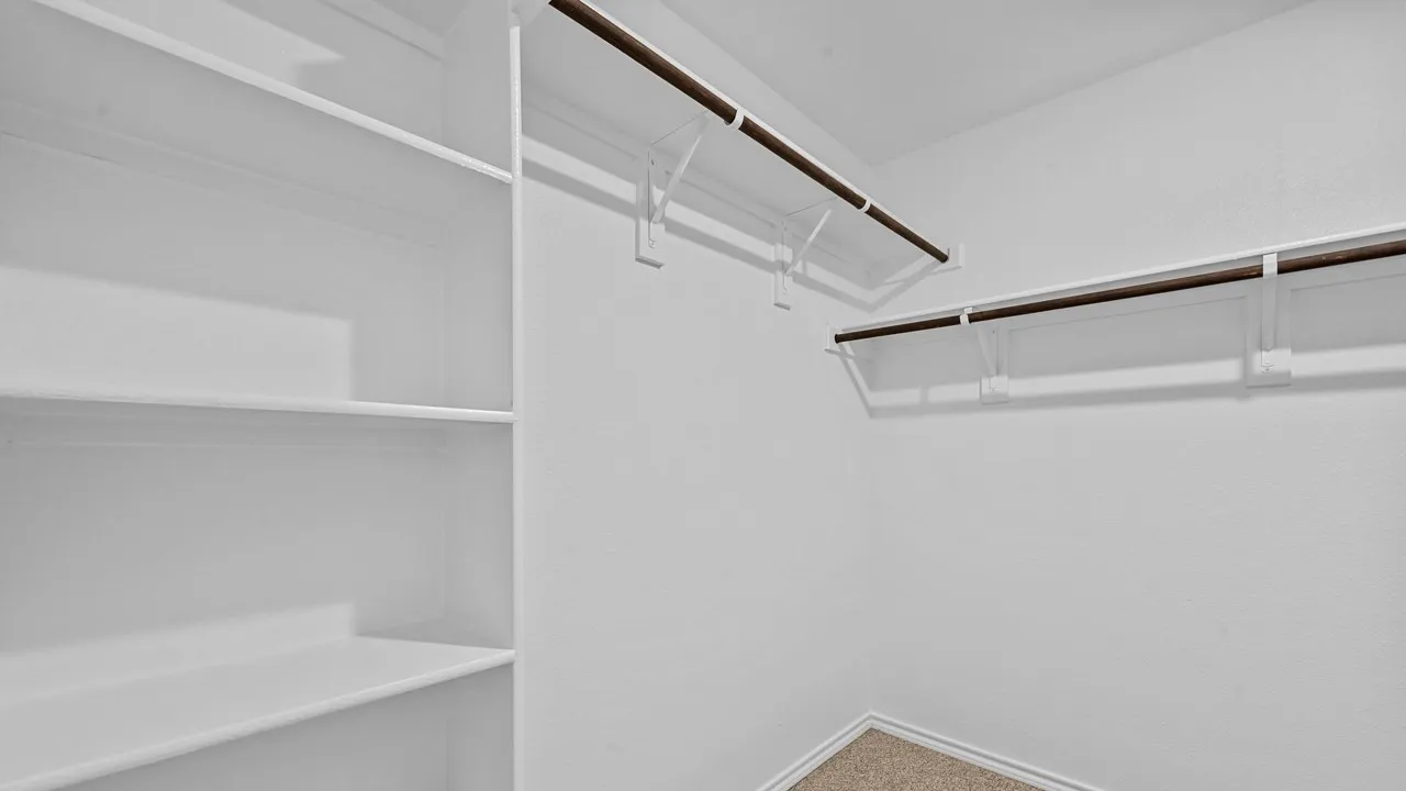 Spacious walk-in closet featuring built-in shelving, dual hanging rods with metal brackets, and wood-finish flooring throughout
