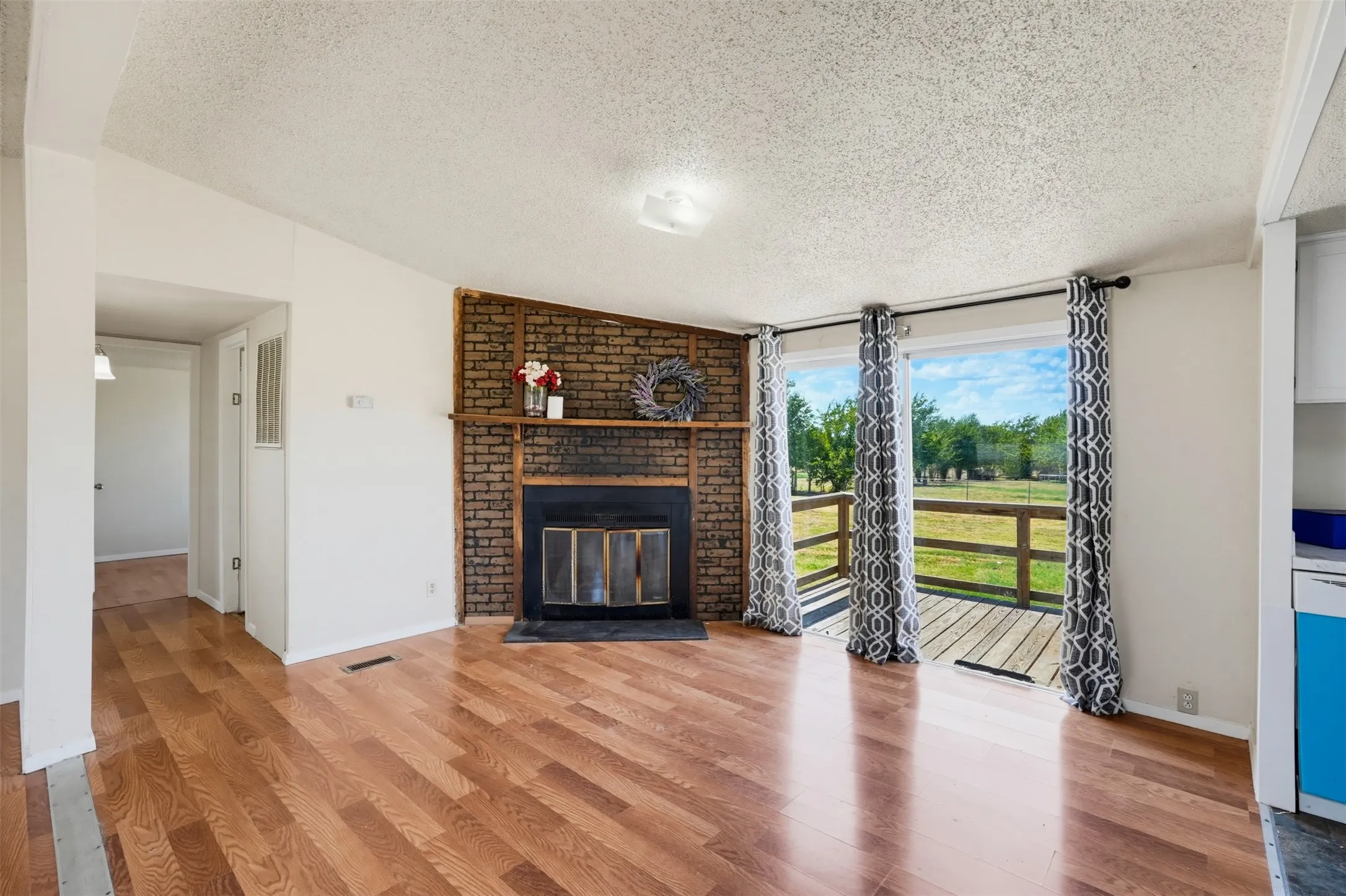 Brick-faced fireplace with a wood mantel, wood-finish flooring, and sliding glass doors leading to an exterior deck