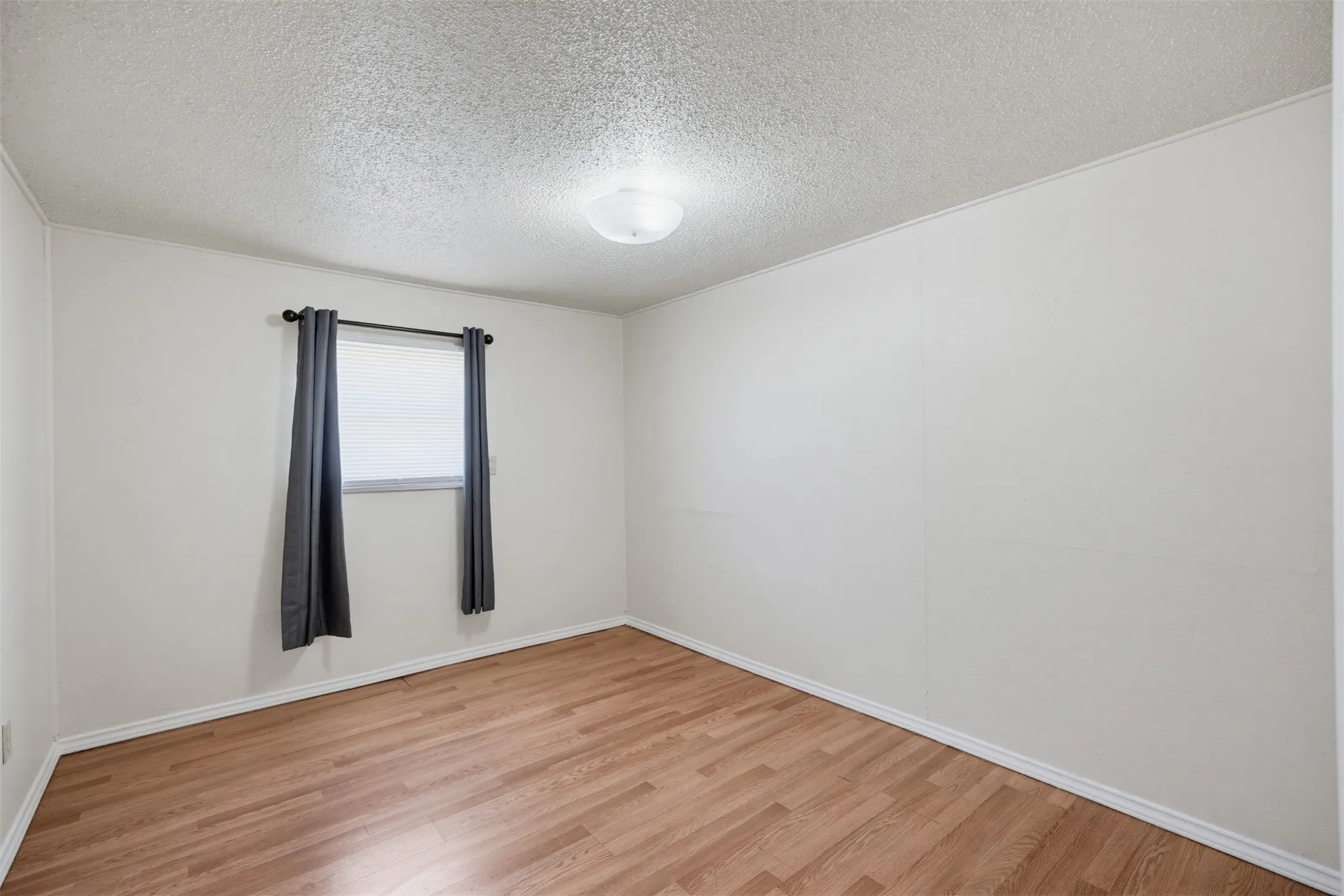 Wood-finish flooring with light-toned walls and a window with blinds