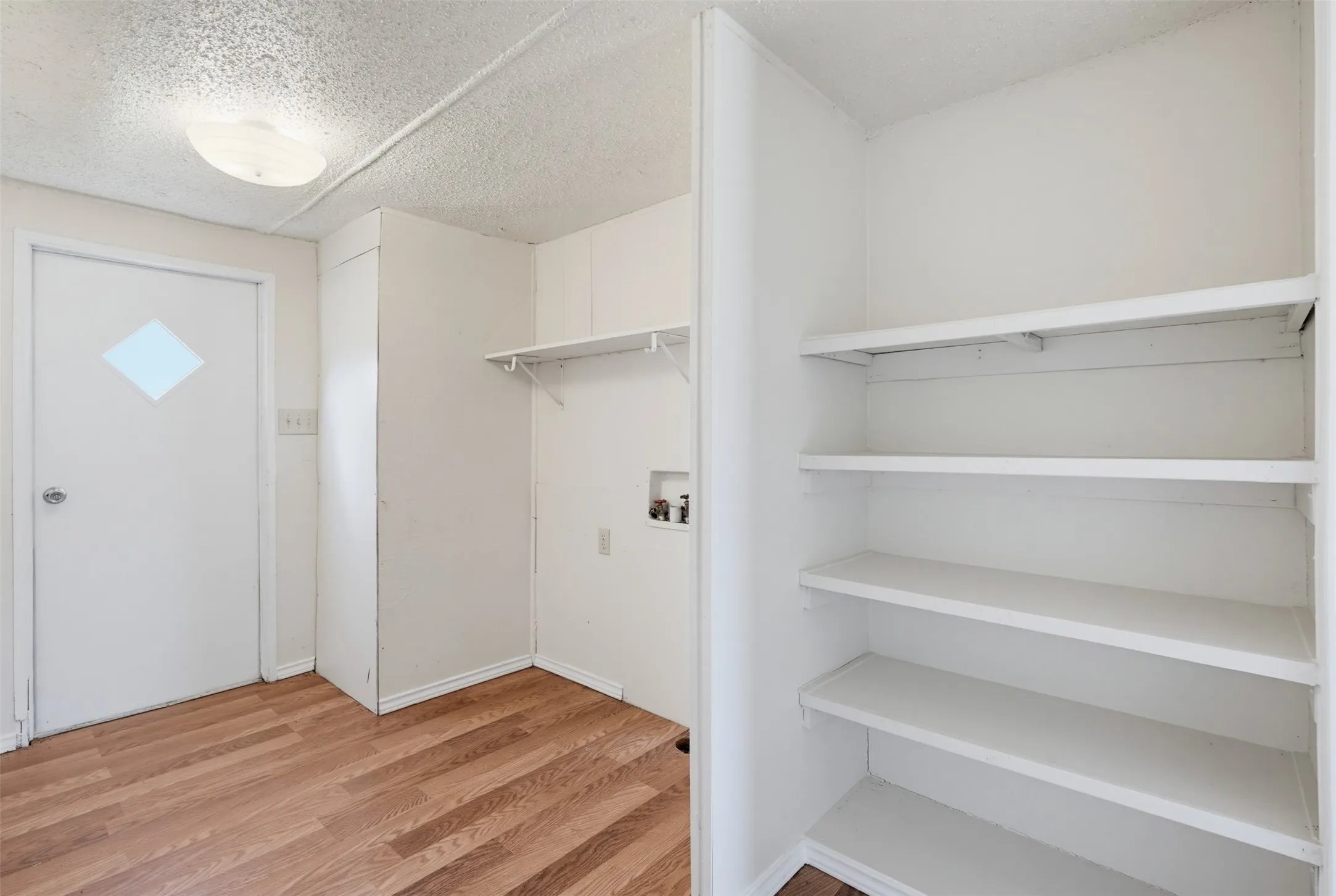 Utility area featuring wood-finish flooring, overhead lighting, and built-in shelving