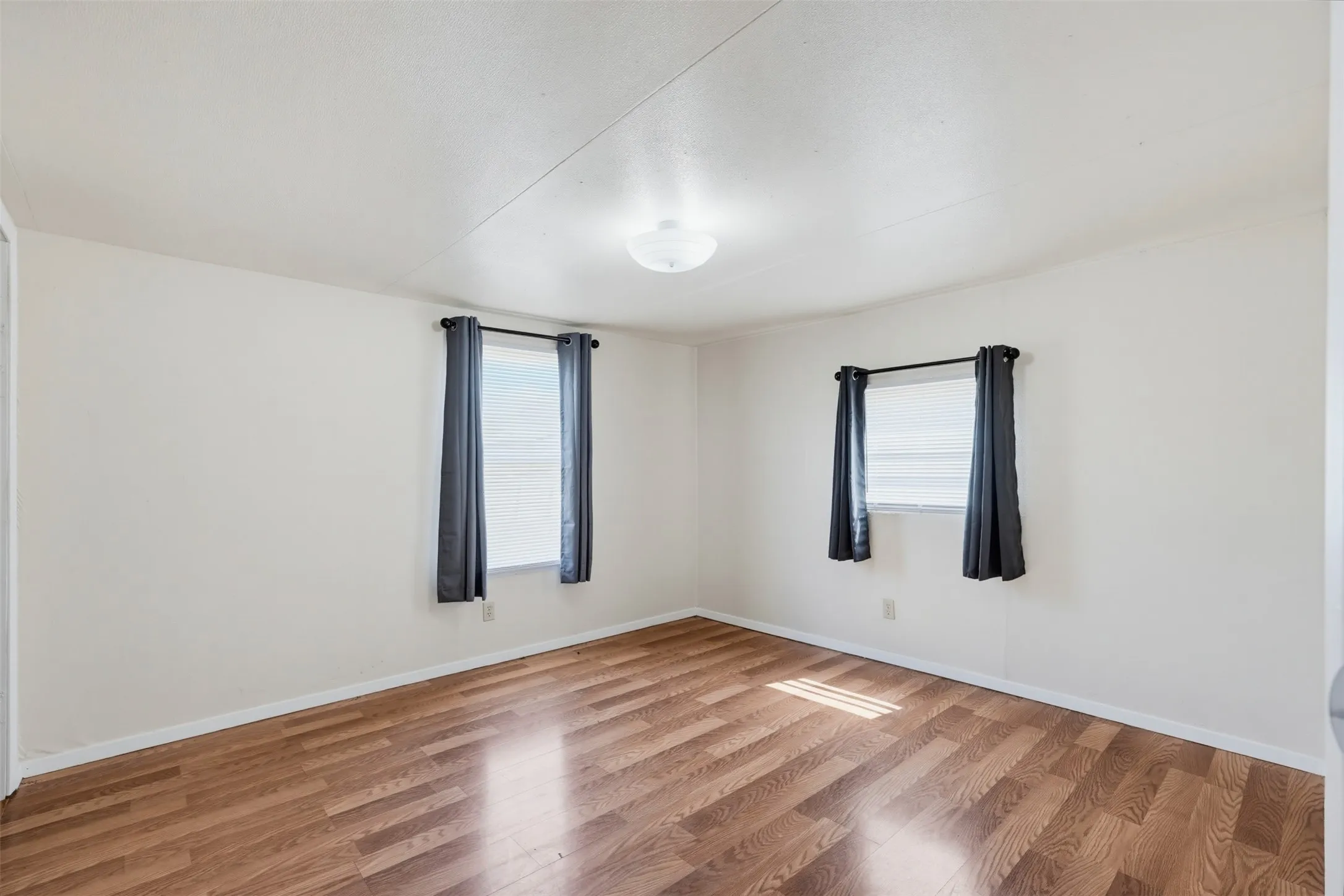 Wood-finish flooring, white walls, two windows, and a ceiling-mounted light fixture