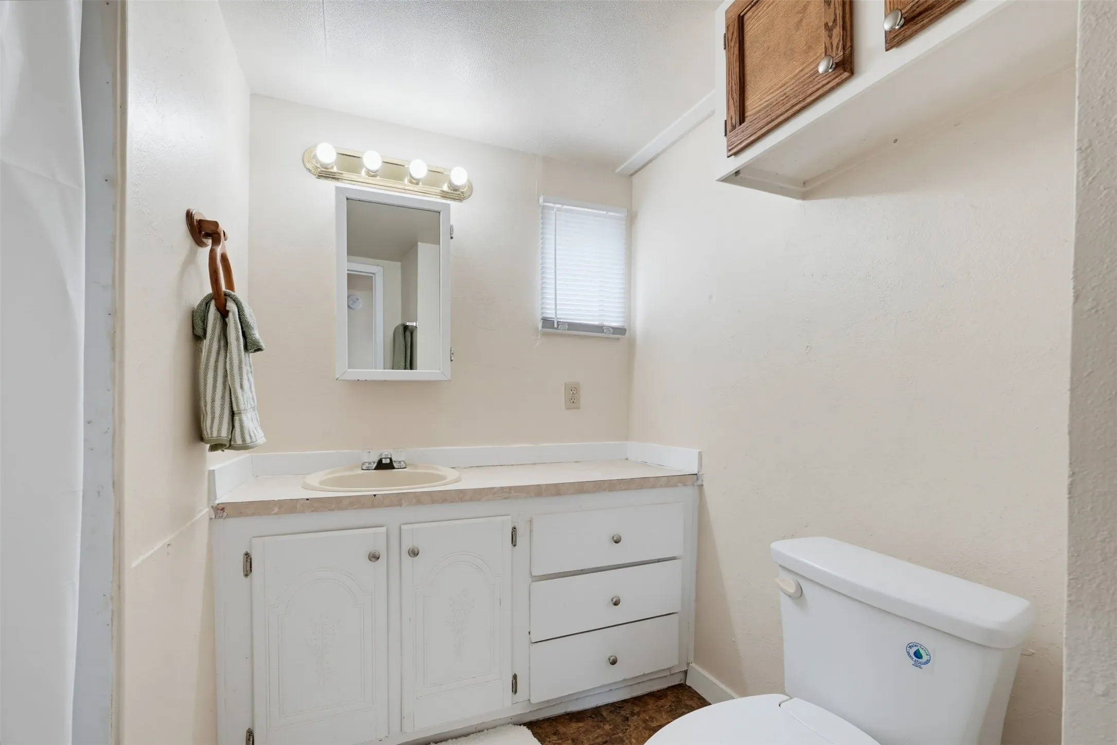 Vanity with an integrated sink, white cabinetry, a wall-mounted mirror, and overhead lighting