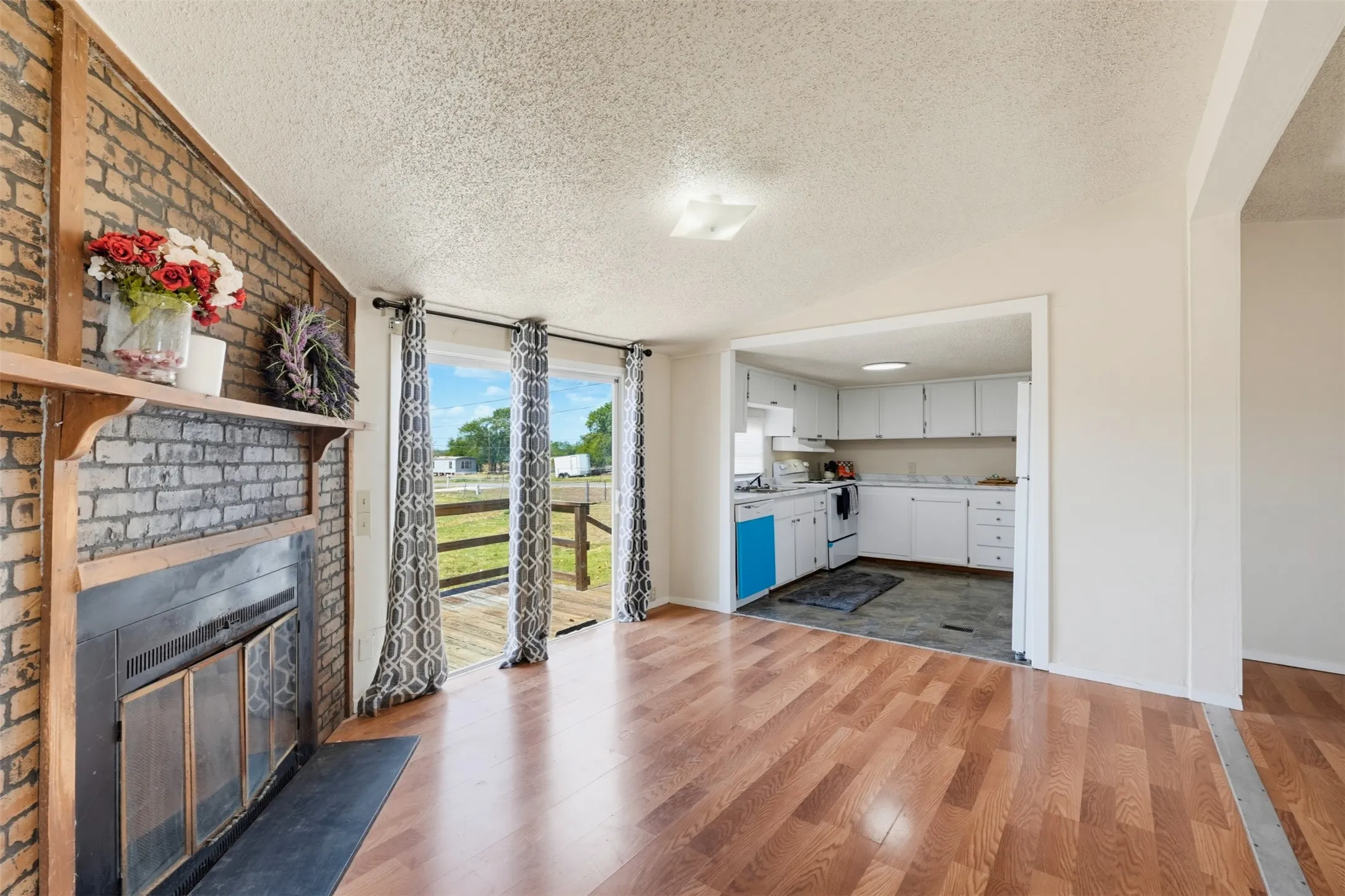 Brick fireplace with wood mantle, wood-finish flooring, sliding glass doors, white kitchen cabinetry, and a built-in kitchen appliance
