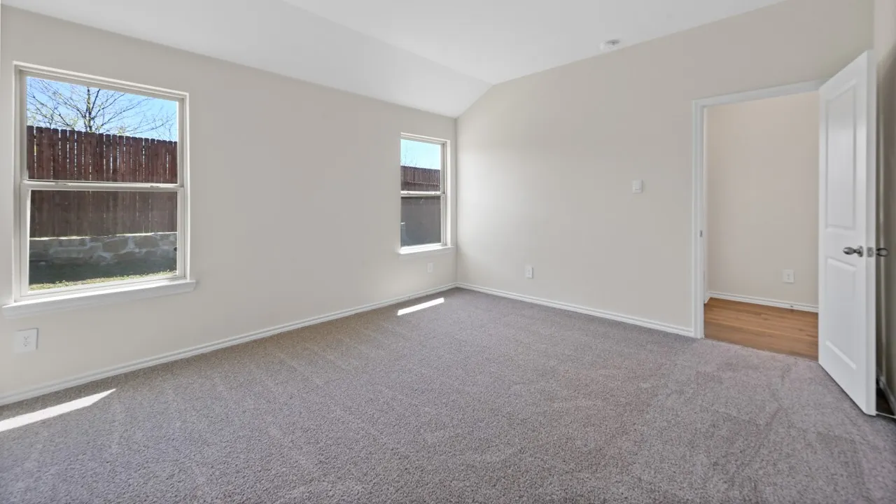Spacious room featuring vaulted ceilings, light gray wall paint, and gray carpet flooring