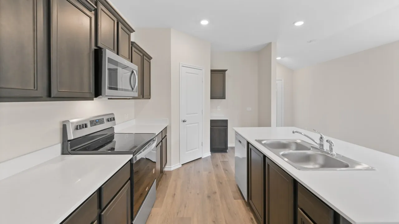 Modern kitchen featuring dark wood cabinetry, light countertops, stainless steel appliances, and wood-finish flooring