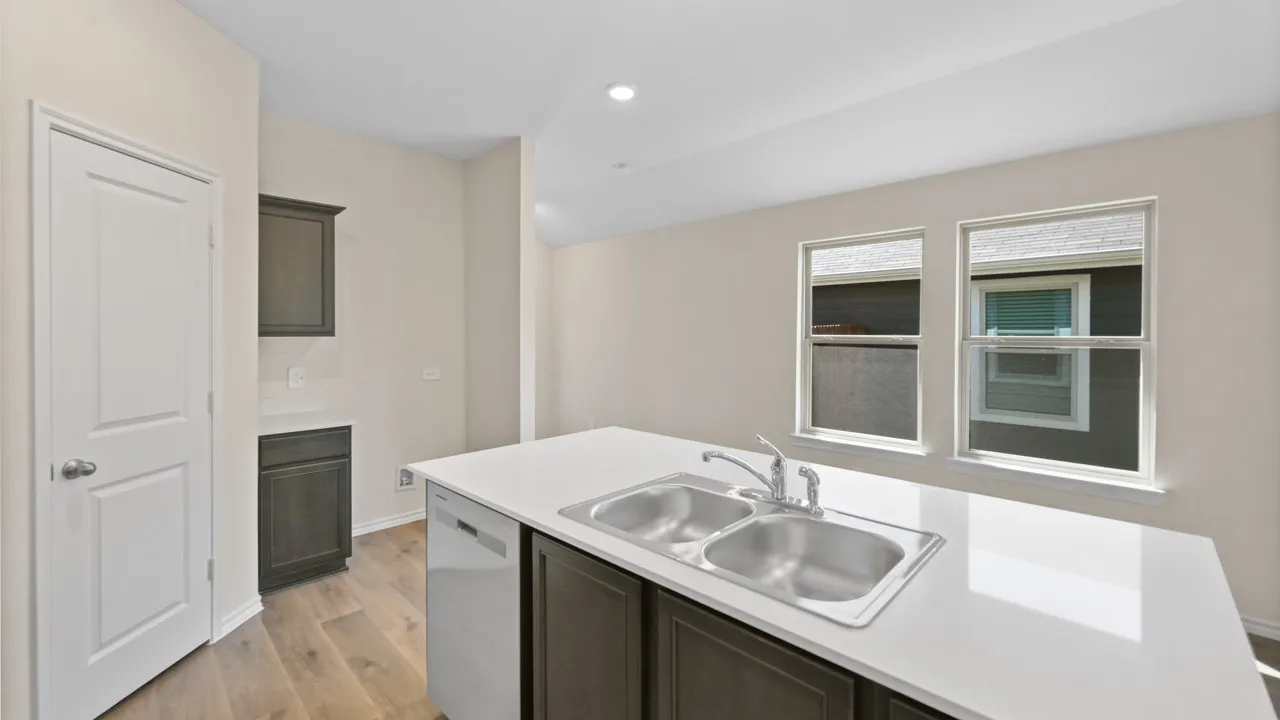 Kitchen island featuring a dual-basin stainless steel sink with a chrome faucet, white countertop, and integrated dishwasher