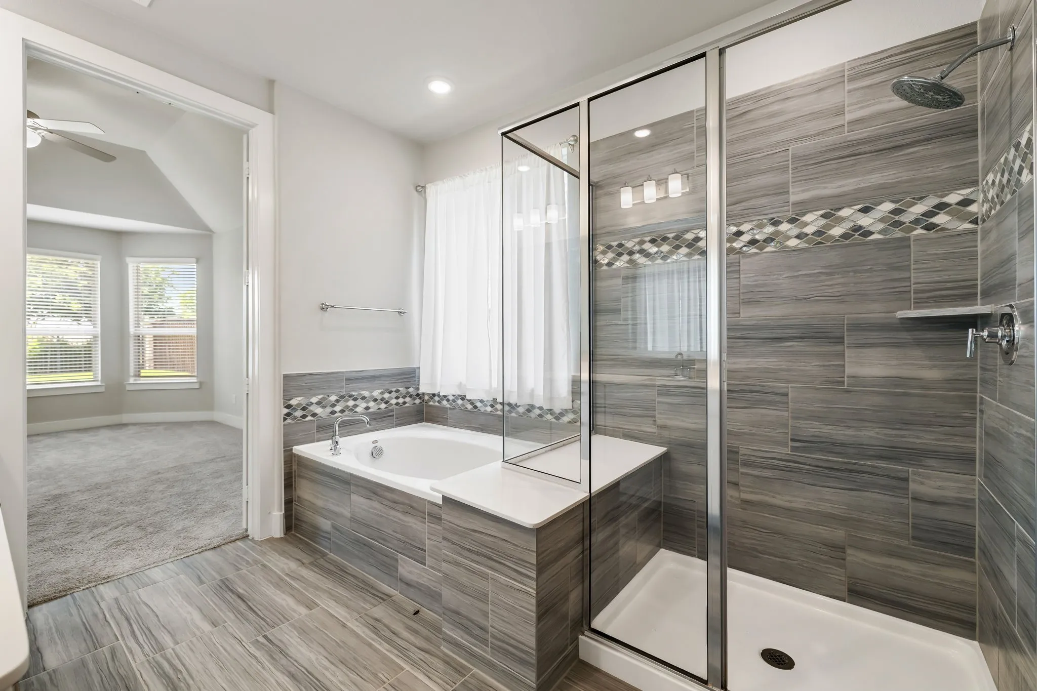 Large soaking tub with tiled surround, separate glass-enclosed shower, wood-look tile flooring, and recessed lighting