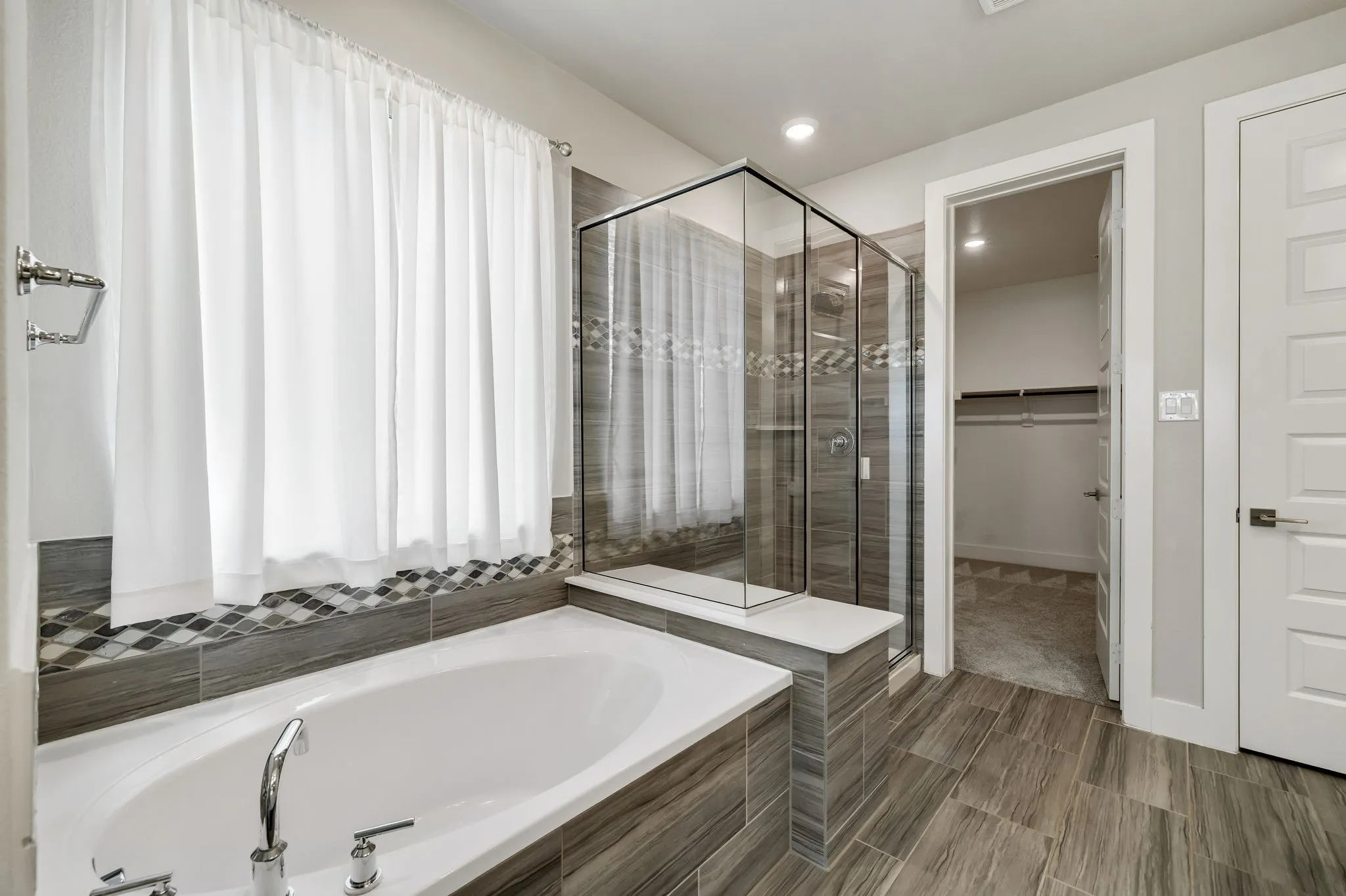 Soaking tub with deck-mounted chrome fixtures, a glass-enclosed shower, tiled shower walls, wood-finish flooring, and a walk-in closet