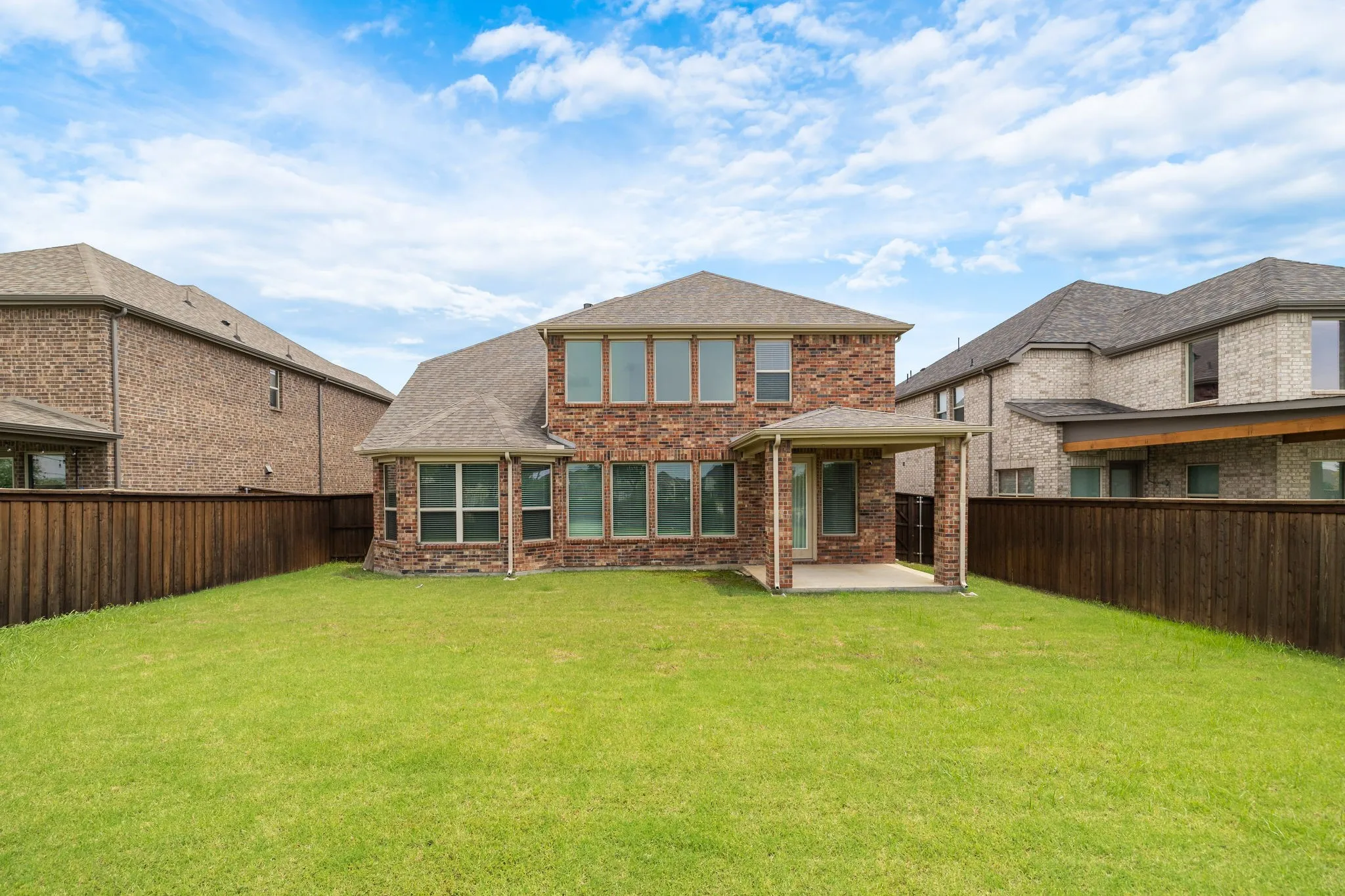 Expansive grassy backyard featuring a covered patio, full privacy fencing, and a brick and stone exterior