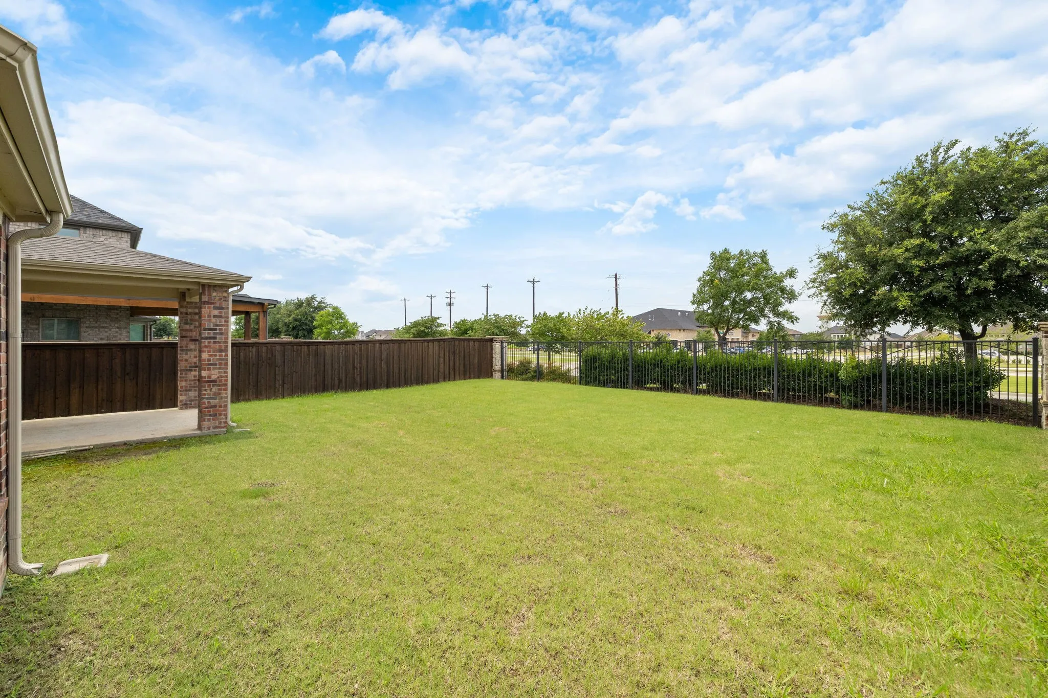 Expansive green lawn with a covered patio, brick columns, and a wood privacy fence